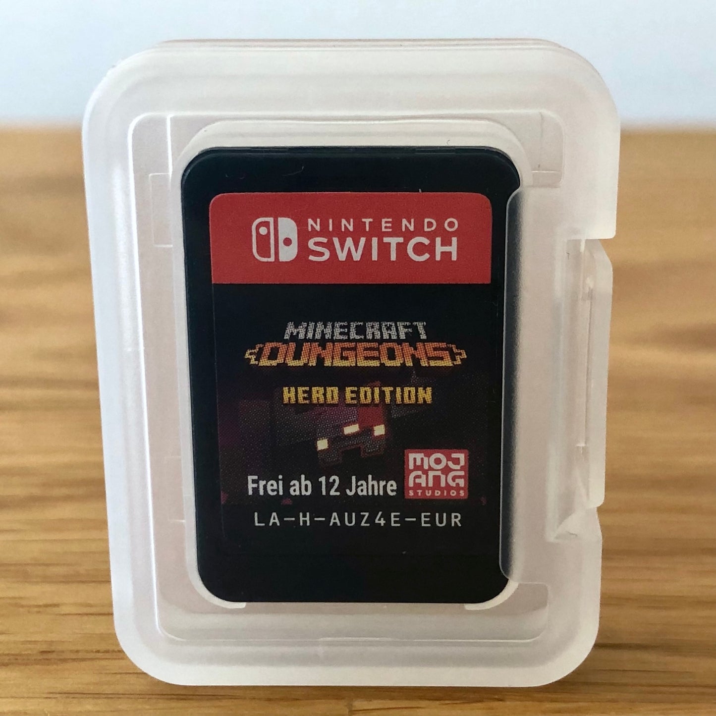 Nintendo Switch game card for Minecraft Dungeons Hero Edition in a clear plastic case on a wooden surface.