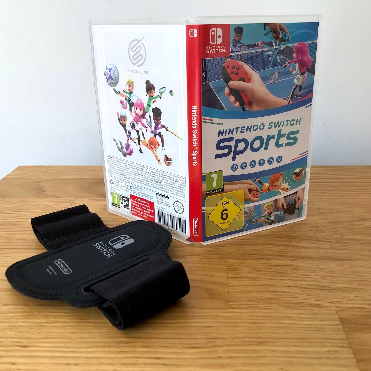 Angled front view of Nintendo Switch Sports for Nintendo Switch, placed on a wooden surface with leg strap in foreground.