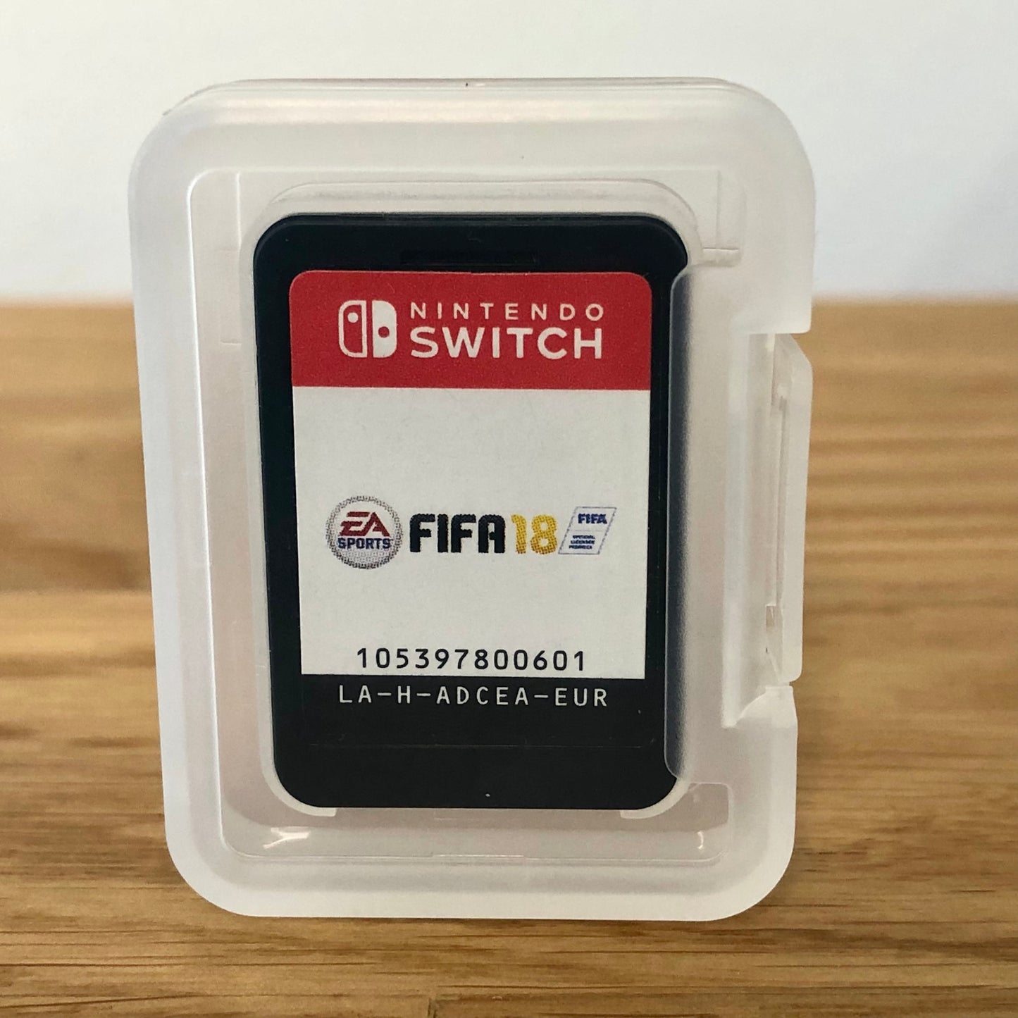 Cartridge of Fifa 18 for Nintendo Switch, the cartridge is inside a cartridge size transparent protective case, through which you can see the front of the cartridge.