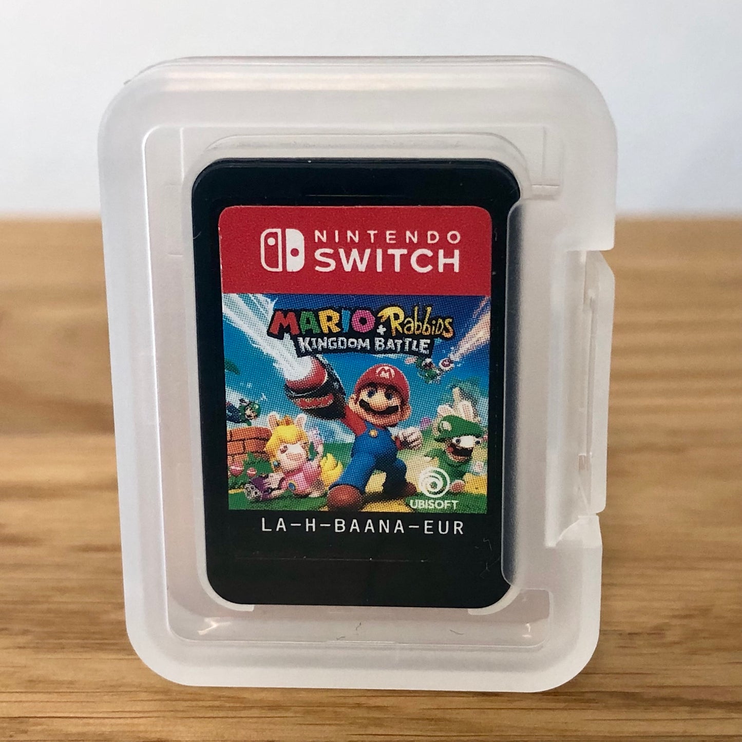 Cartridge of Mario + Rabbids Kingdom Battle for Nintendo Switch, the cartridge is inside a cartridge size transparent protective case, through which you can see the front of the cartridge