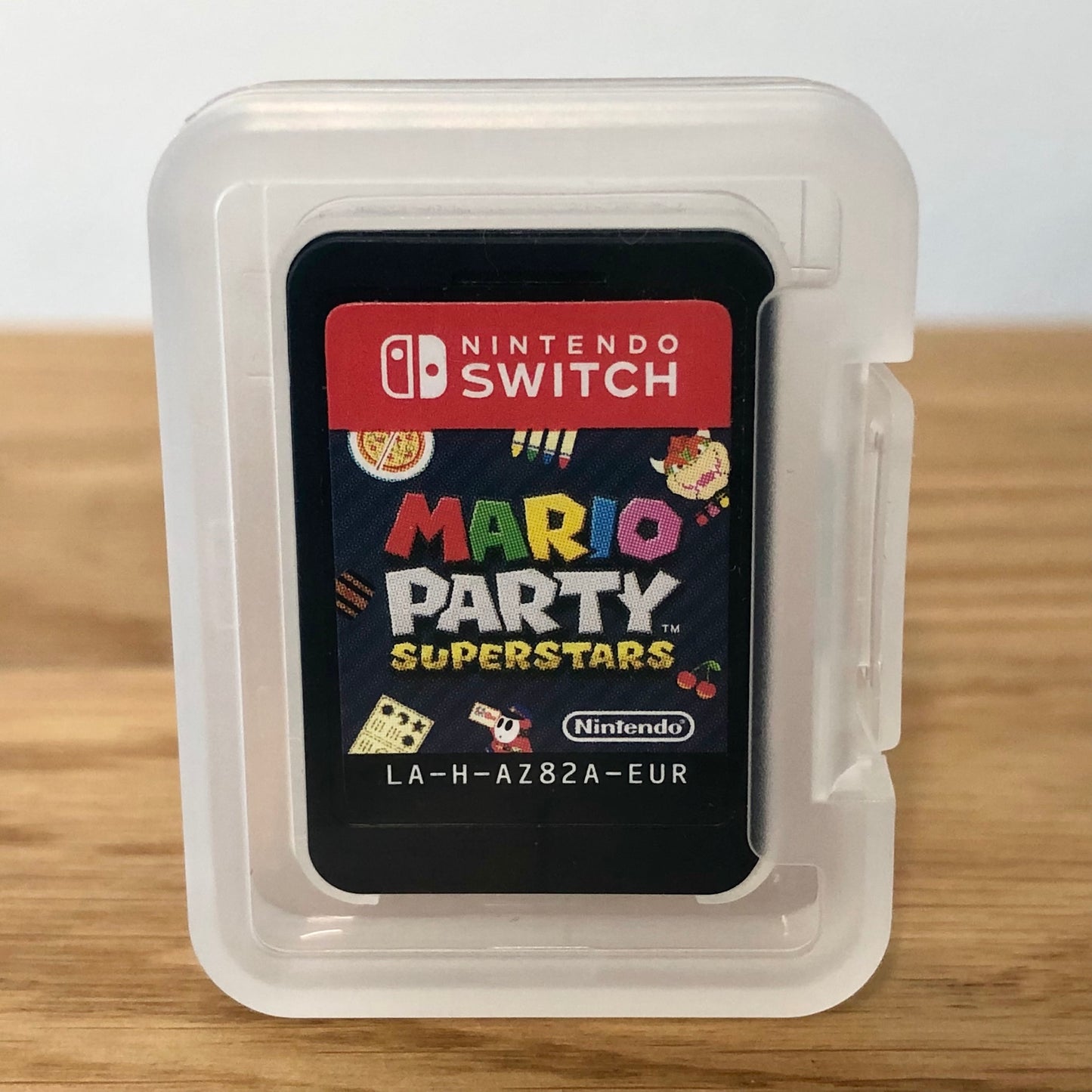 Cartridge of Mario Party Superstars for Nintendo Switch, the cartridge is inside a cartridge size transparent protective case, through which you can see the front of the cartridge