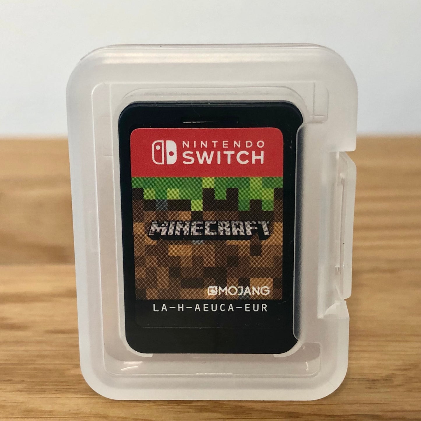 Nintendo Switch game card with Minecraft branding in a clear plastic case on a wooden surface.