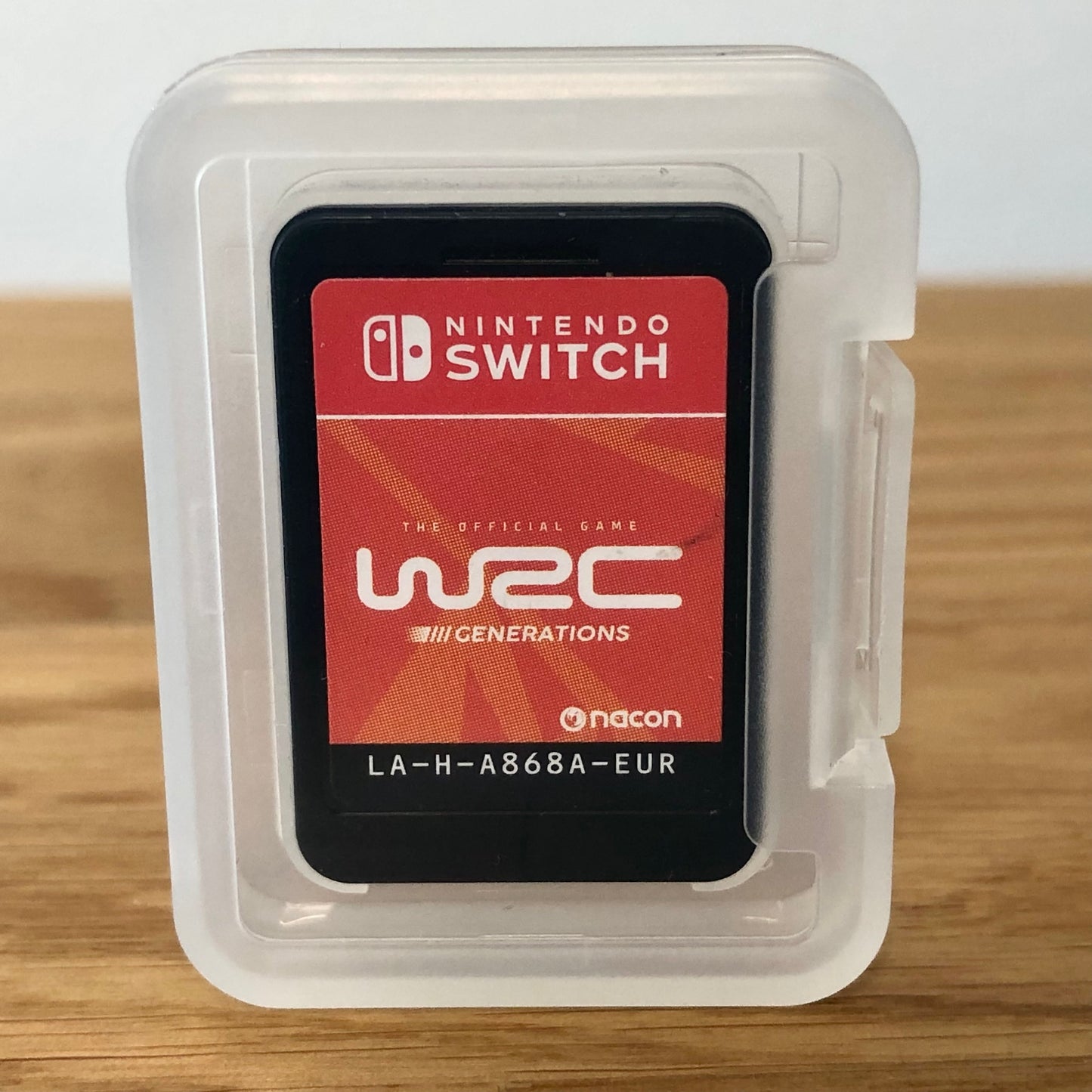 Cartridge of WRC Generations for Nintendo Switch, the cartridge is inside a cartridge size transparent protective case, through which you can see the front of the cartridge