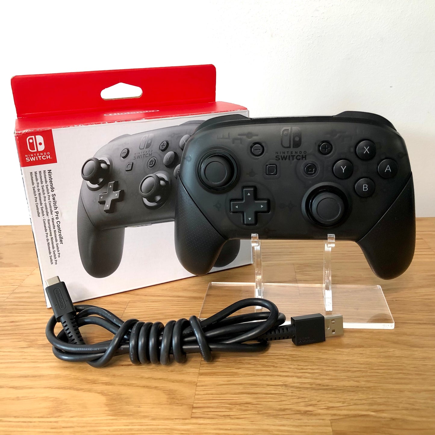 Front view of Nintendo Switch Pro Controller, showing button layout and ergonomic design. Also shows pro controller box and type-c charger cable
