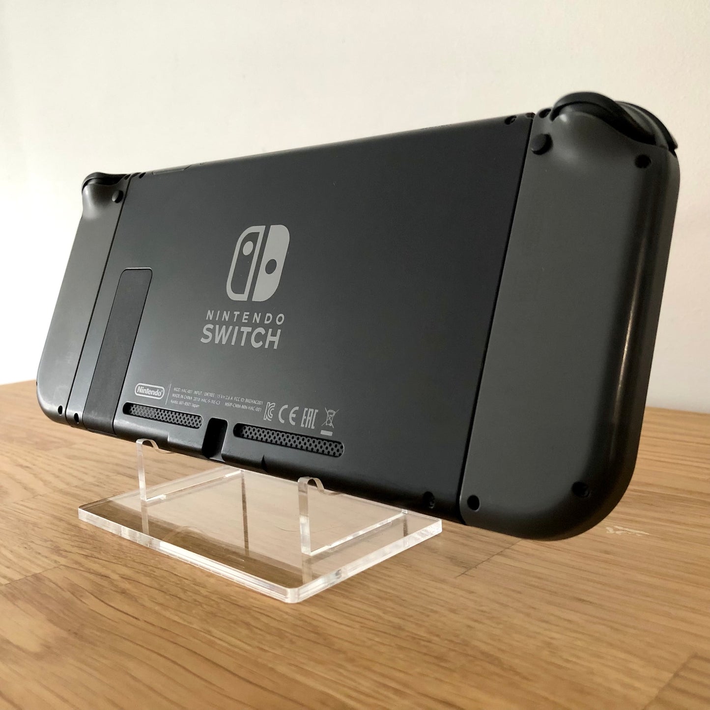 Back angled view of Nintendo Switch console with grey Joy-Cons attached, showing logo, kickstand and trigger buttons.