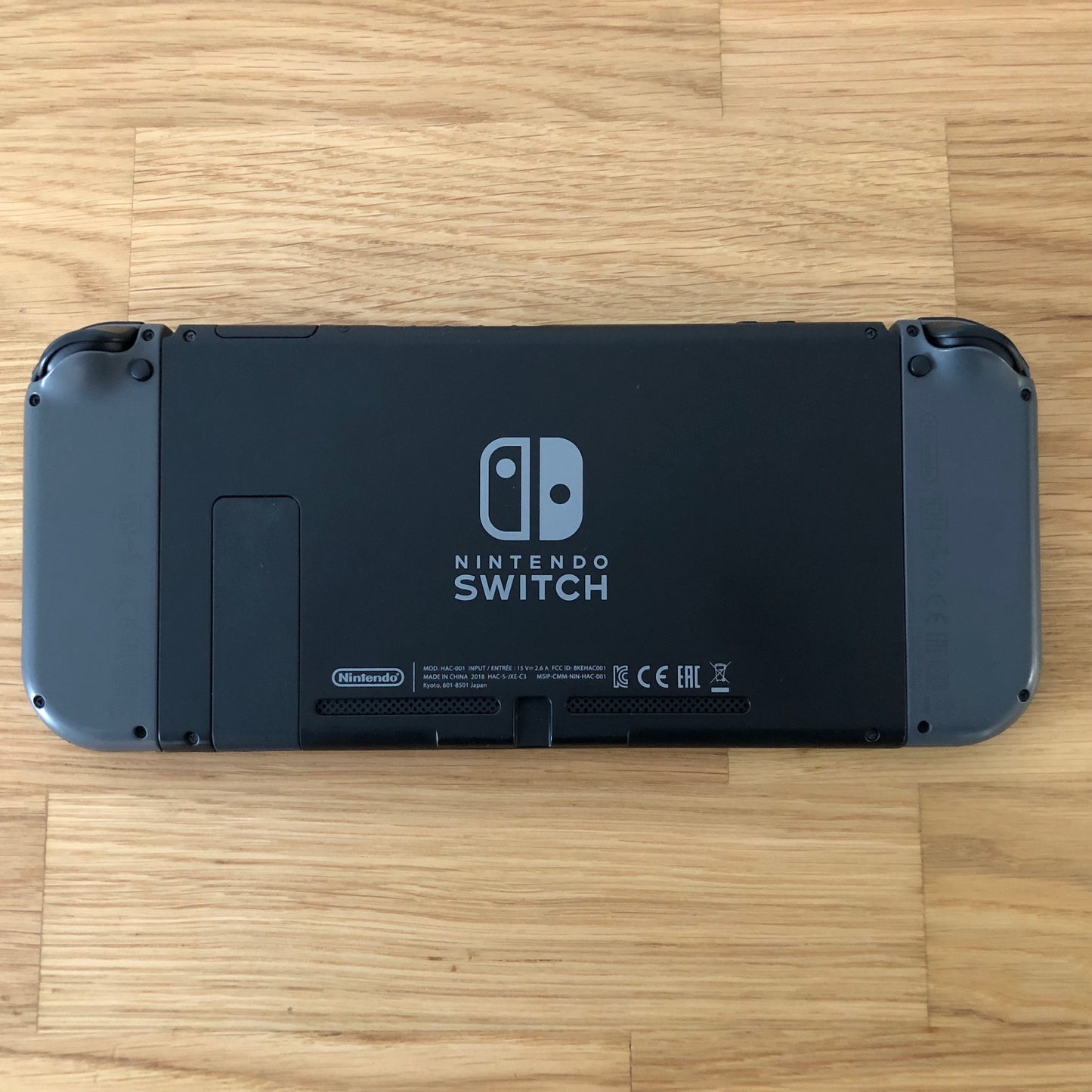 Back of Nintendo Switch console with Joy-Cons attached, showing logo, serial info, triggers and kickstand. Laid flat