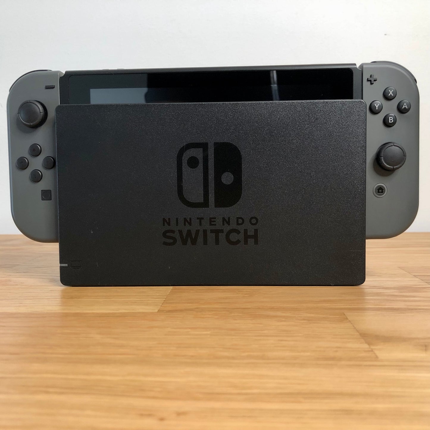 Front of grey Nintendo Switch console docked, showing Joy-Cons with all face buttons and screen edge visible.