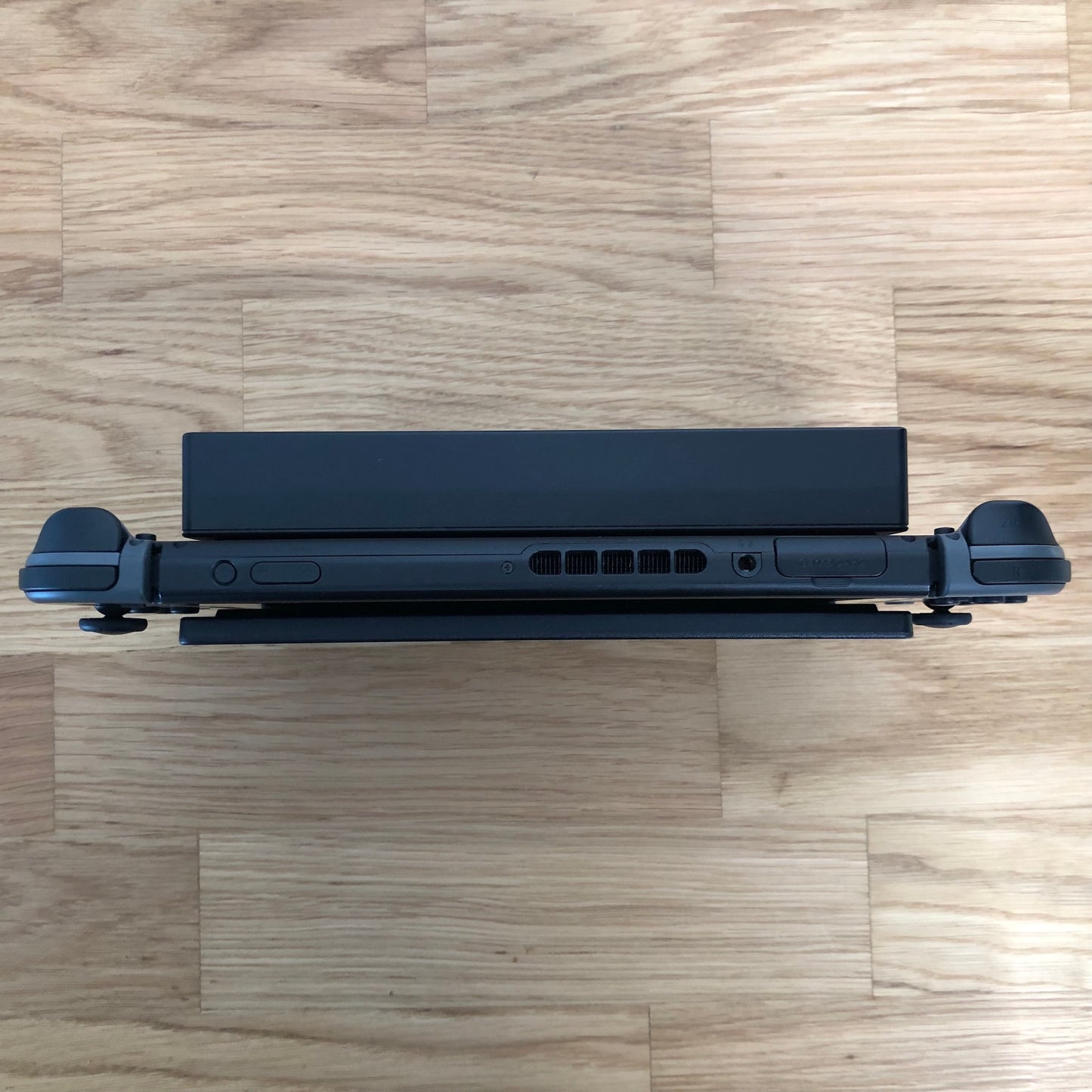 Top-down view of grey Nintendo Switch in dock, showing triggers, volume, power and game card slot.