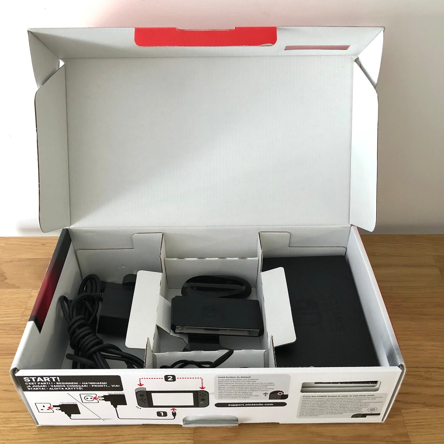 Second layer of Nintendo Switch box showing dock, Joy-Con grip, HDMI cable, charger and straps securely packed.