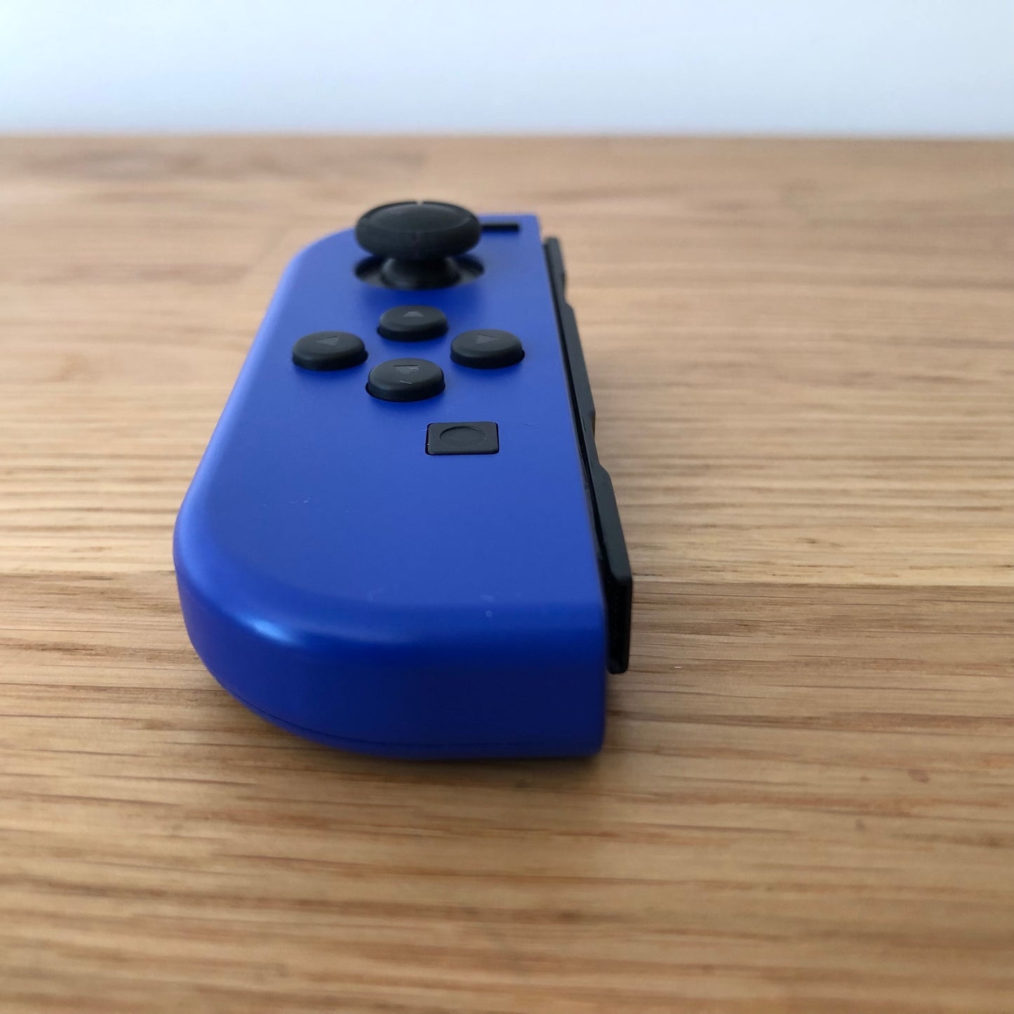 Angled front view of neon blue Nintendo Switch Joy-Con controller showing joystick and minus button.