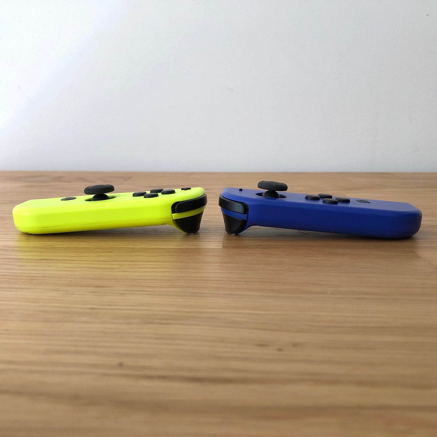 Side view of neon yellow and blue Nintendo Switch Joy-Con controllers resting on a wooden surface