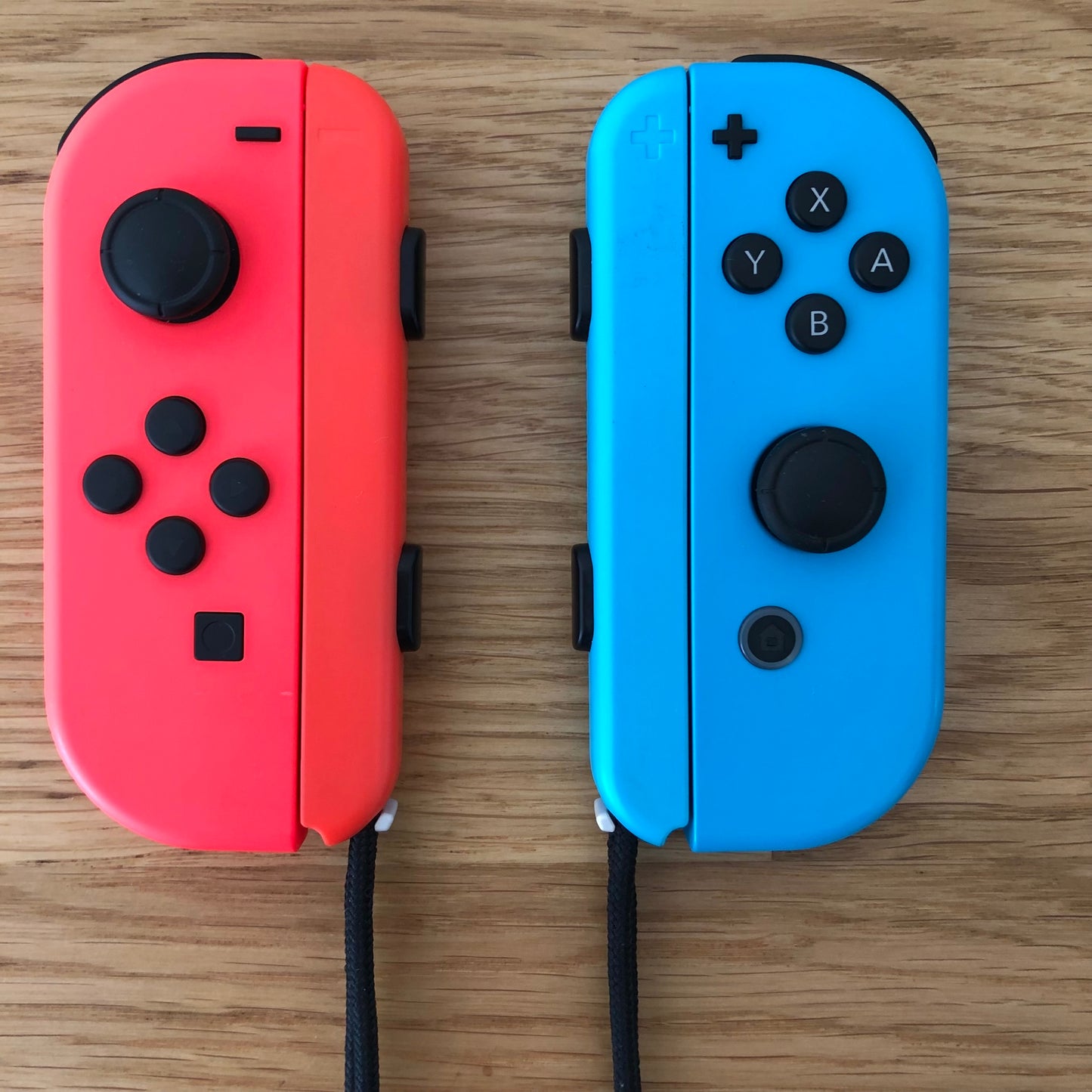 Birds eye top view of Neon Red & Blue Joy-Cons pair with supporting wrist straps attached, showing button layout and design.
