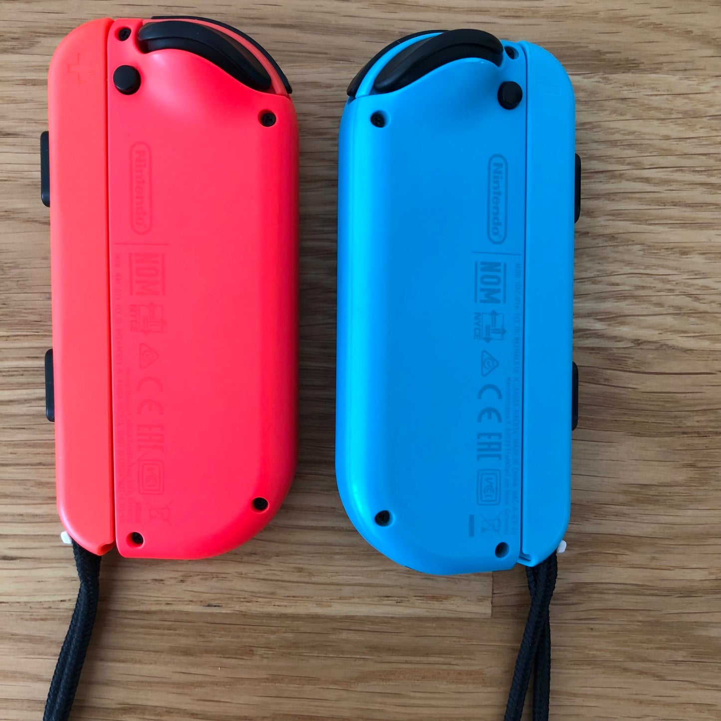 Back view of individual neon red and blue Nintendo Switch Joy-Con controllers side by side on a table.