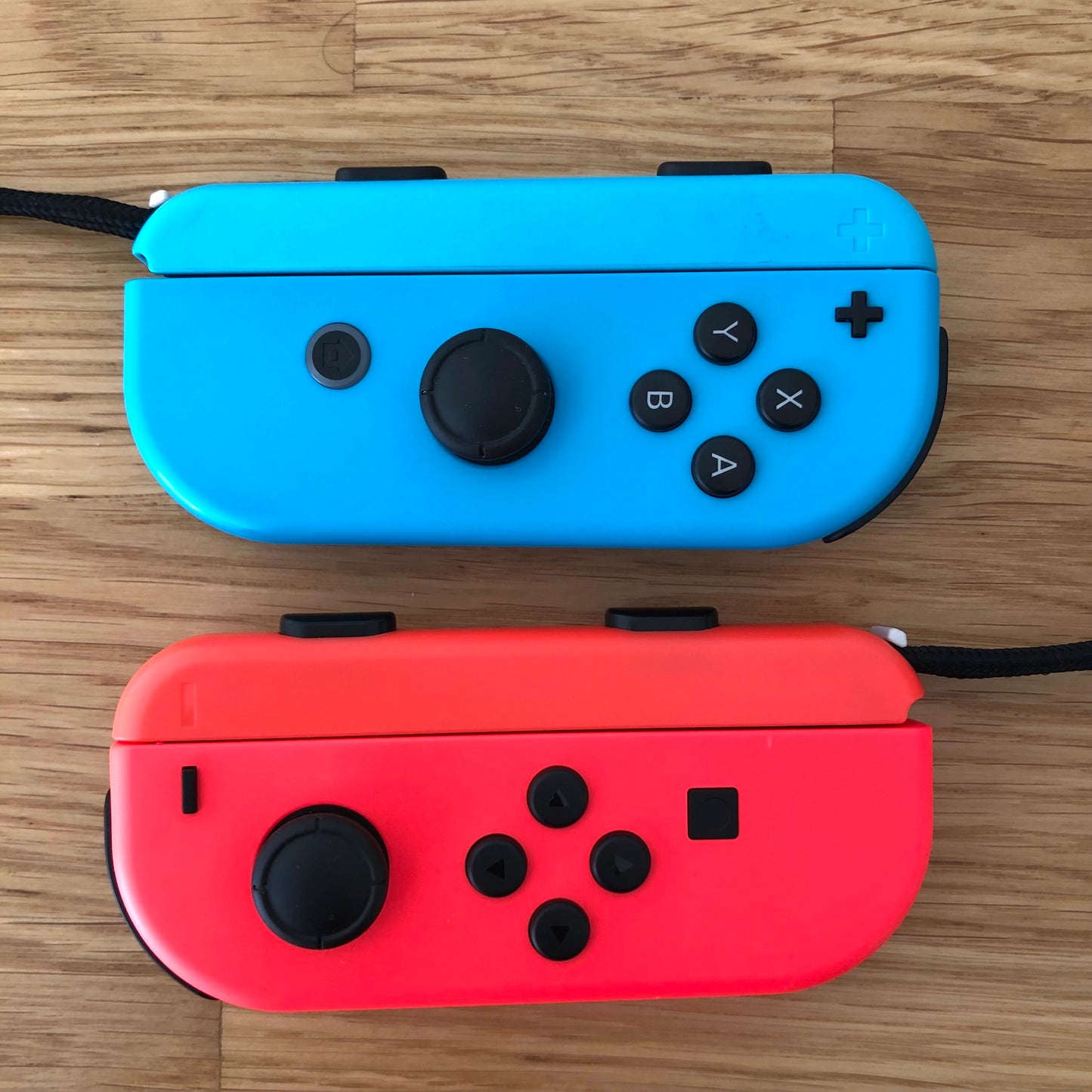 Top-down view of neon red and blue Nintendo Switch Joy-Con controllers side by side on wooden surface.