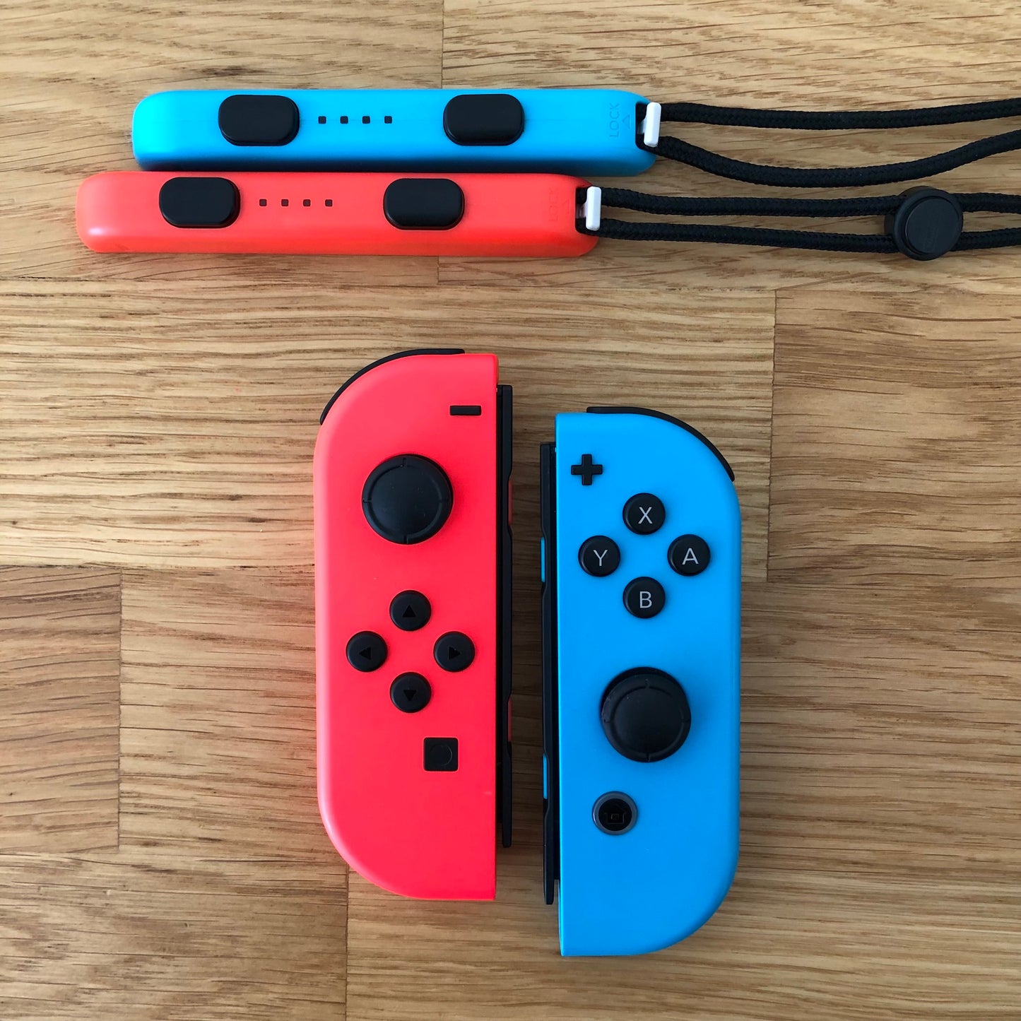 Birds eye top view of Neon Red & Blue Joy-Cons pair with supporting wrist straps attached, showing button layout and design.