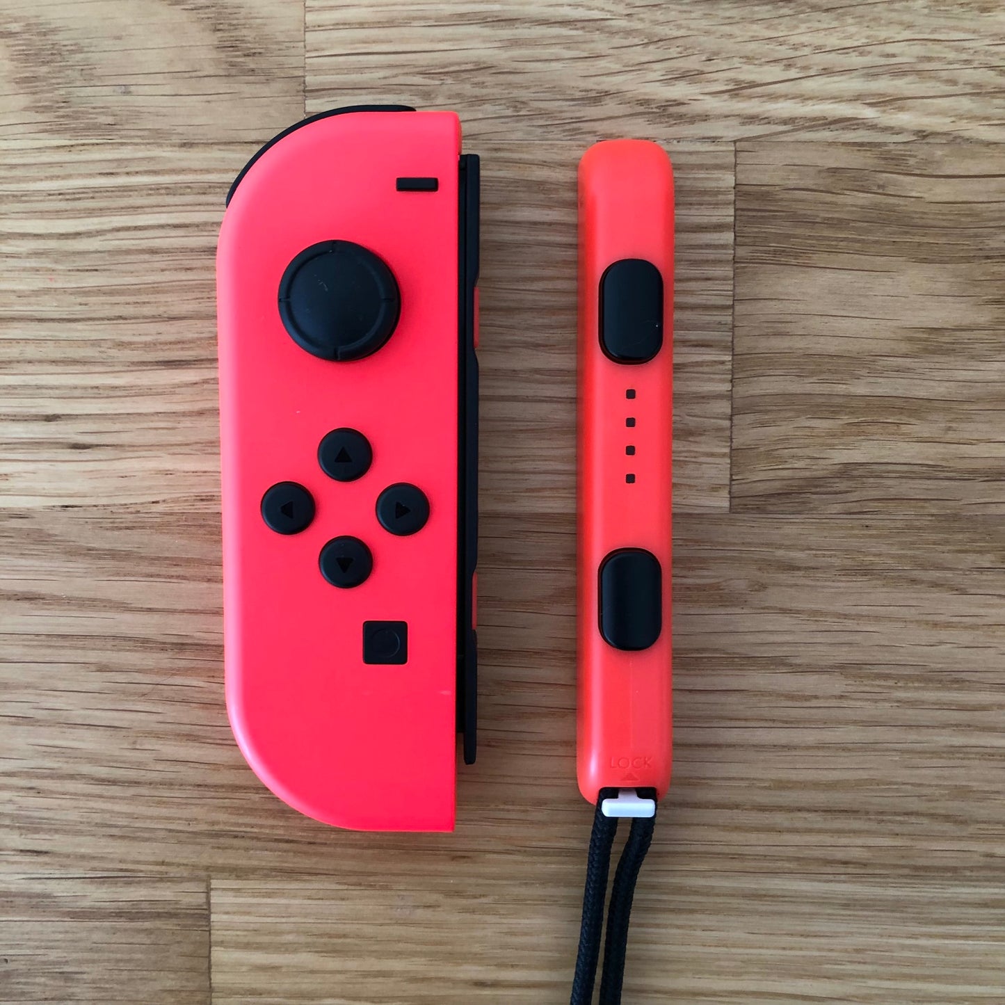 Top-down view of neon red Joy-Con controller and matching wrist strap for Nintendo Switch on wooden surface.