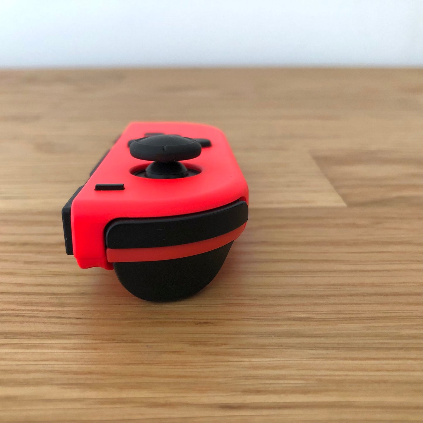Close-up front angle of neon red Nintendo Switch Joy-Con controller showing control stick and shoulder button.