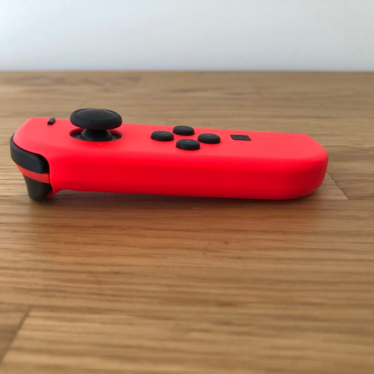 Side profile of neon red Nintendo Switch Joy-Con controller lying flat, showing buttons and curved design.