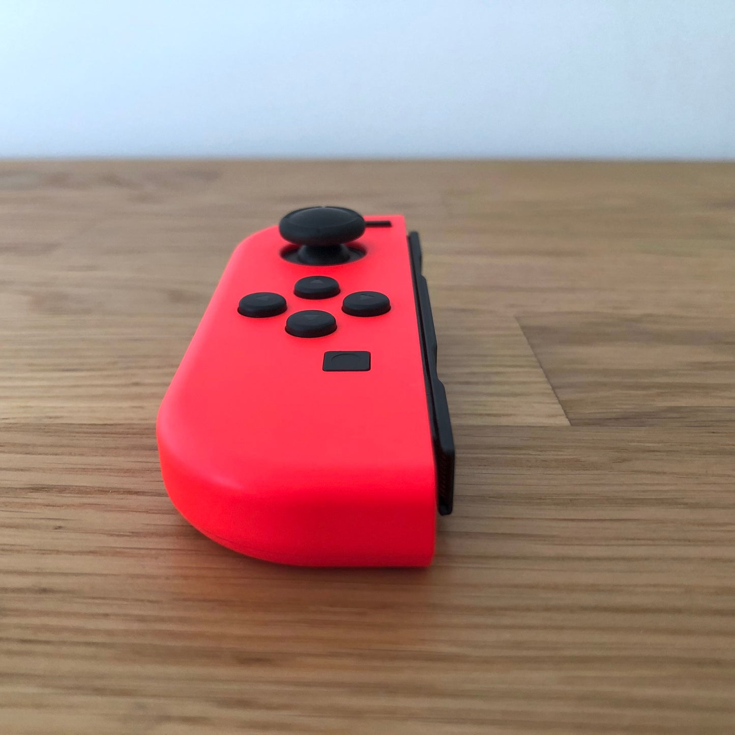 Angled side view of neon red Nintendo Switch Joy-Con controller highlighting joystick and front buttons.