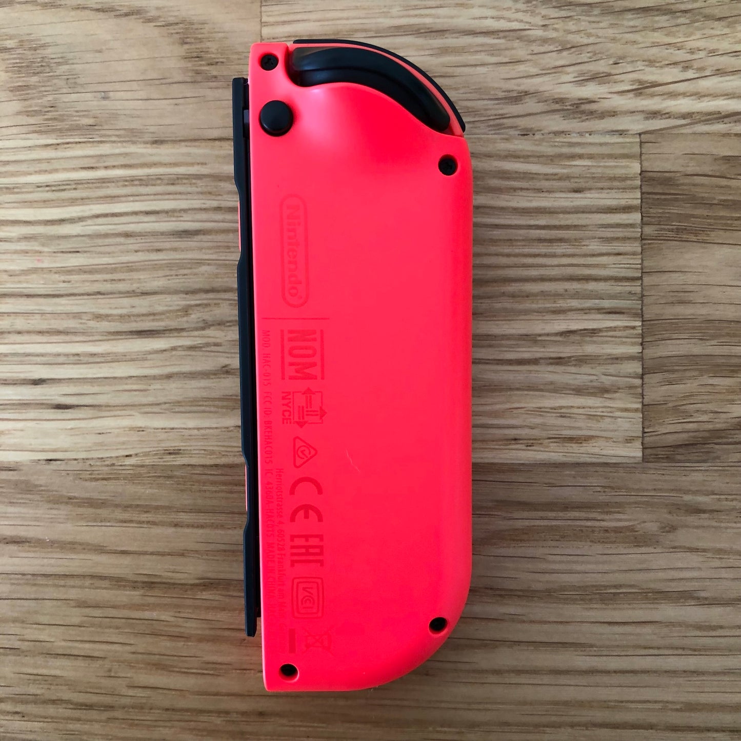 Rear view of neon red Nintendo Switch Joy-Con controller displaying branding and safety markings.