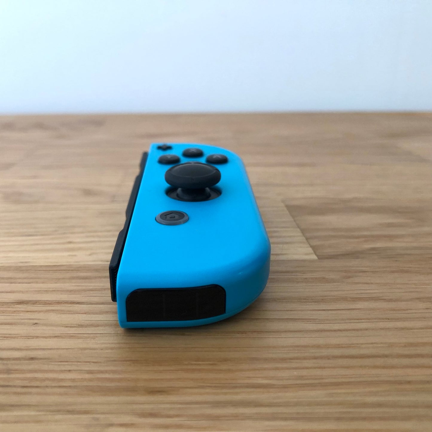 Angled front view of neon blue Nintendo Switch Joy-Con controller showing joystick and minus button.”