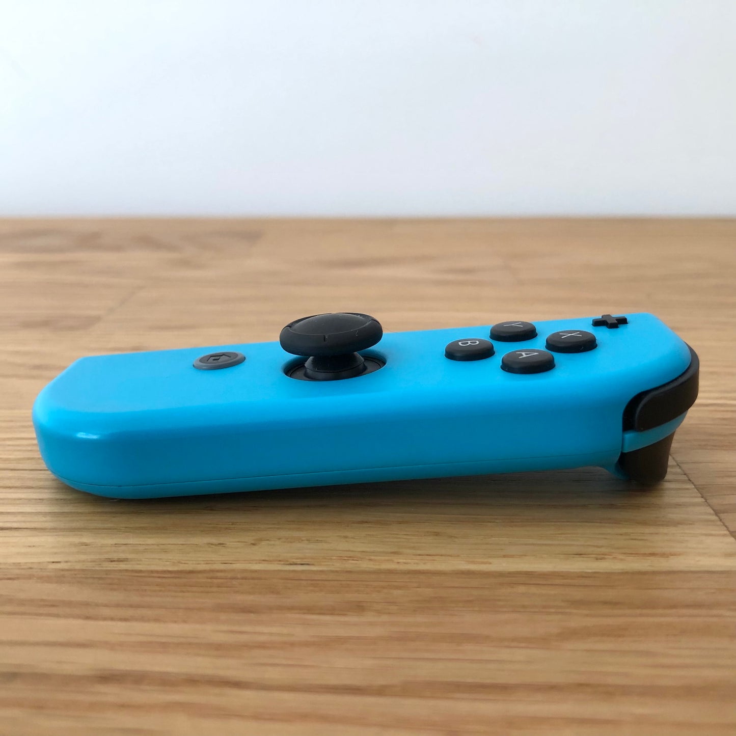 Side profile of neon blue Nintendo Switch Joy-Con controller showing buttons and joystick on wooden surface.