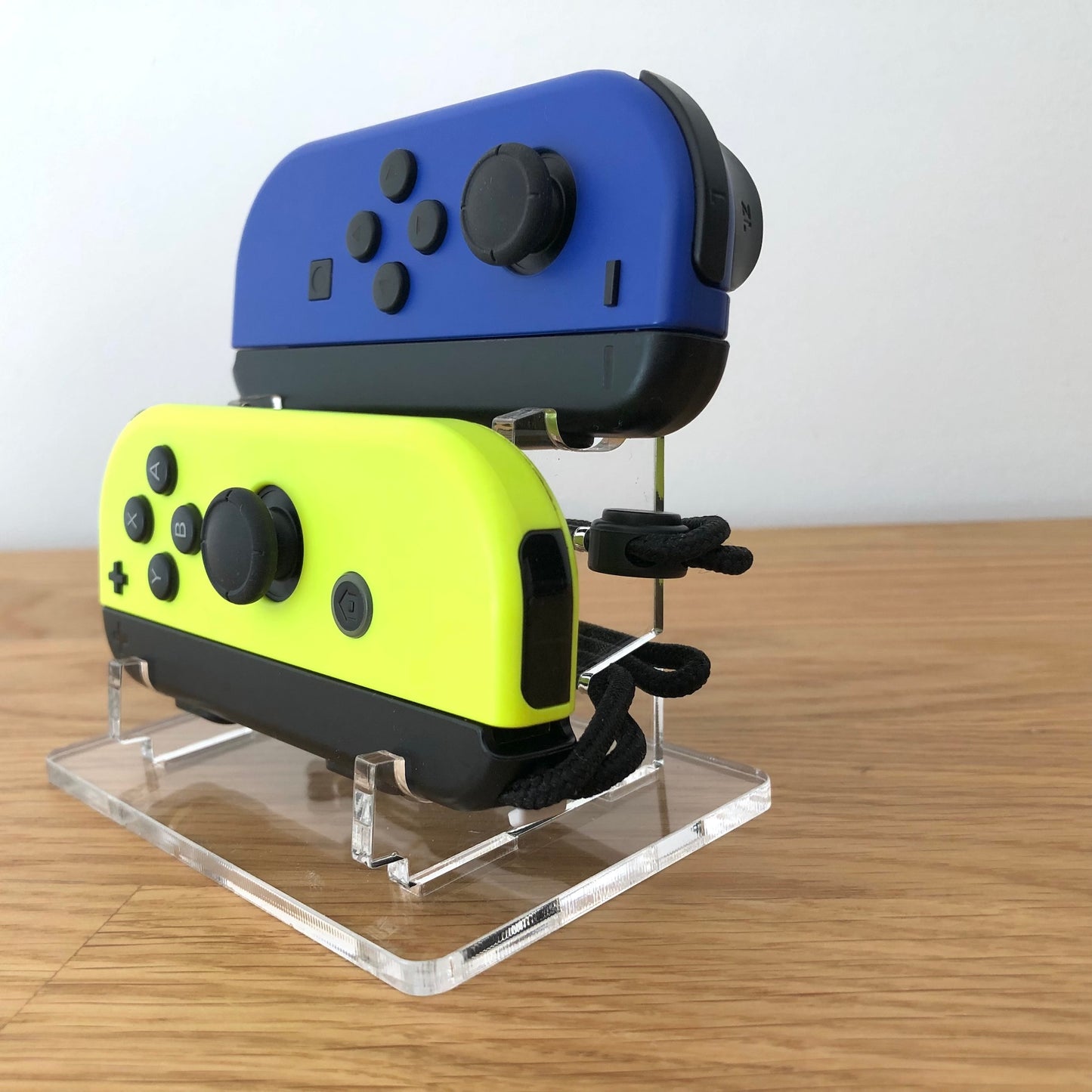 Front view of neon blue and yellow Nintendo Switch Joy-Con controllers displayed vertically on clear stand.