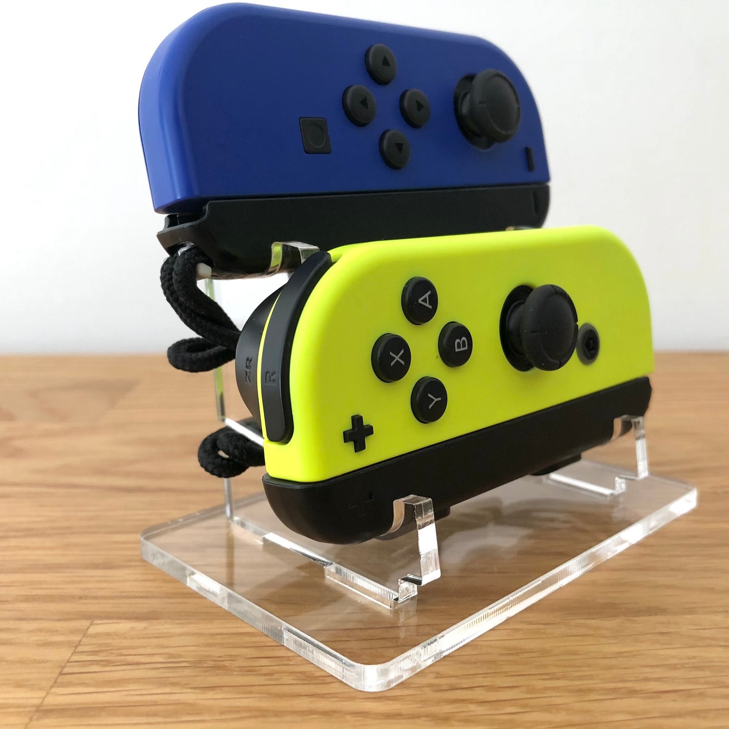 Side angle of neon blue and yellow Nintendo Switch Joy-Cons, displayed on a clear acrylic stand.