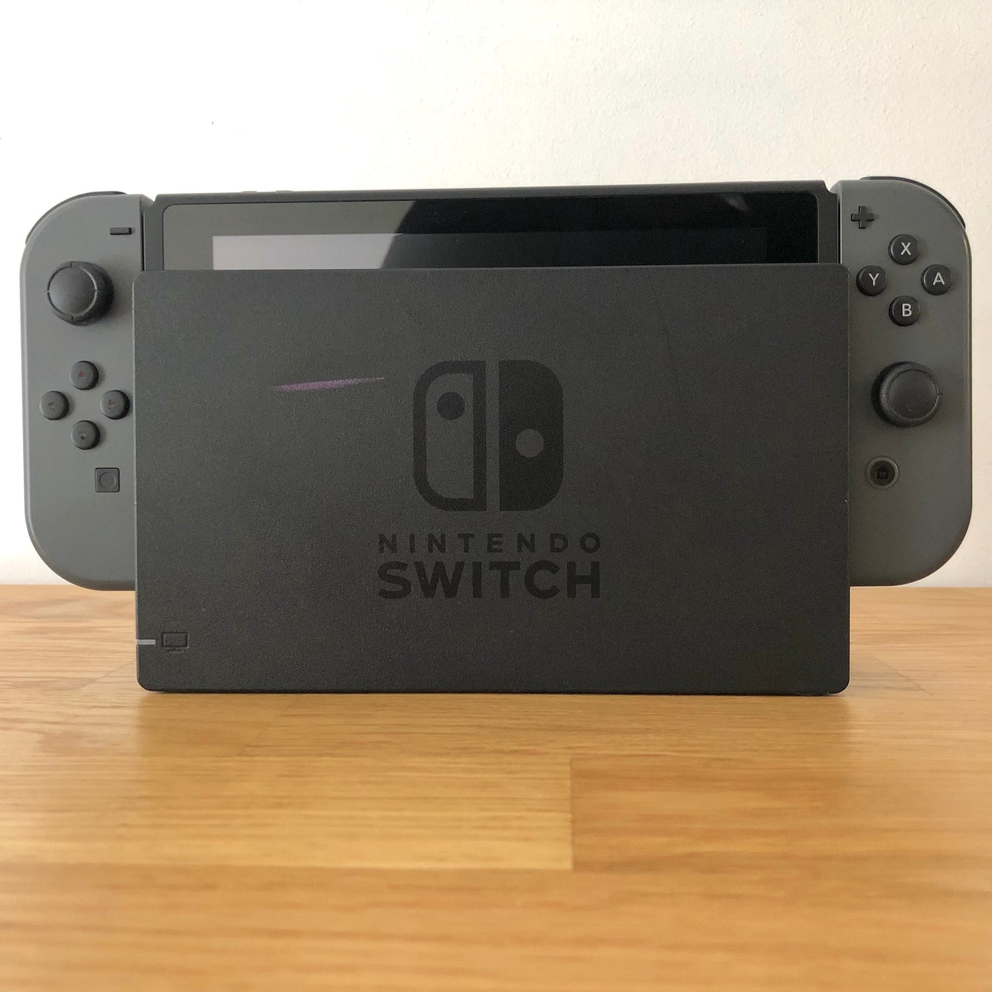 Front of grey Nintendo Switch console docked, showing Joy-Cons with all face buttons and screen edge visible.