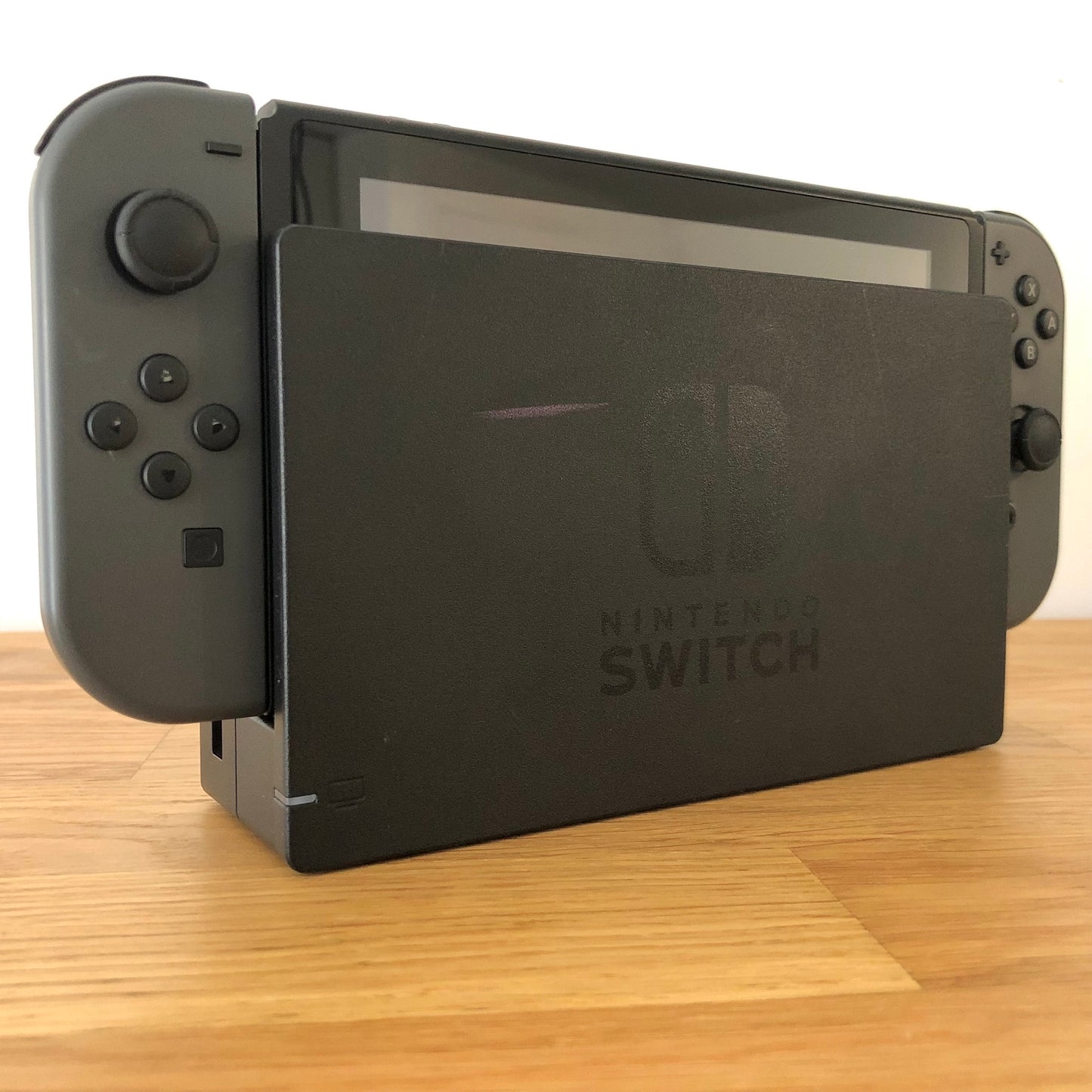 Angled left view of grey Nintendo Switch console docked, showing control sticks and front buttons of Joy-Cons.