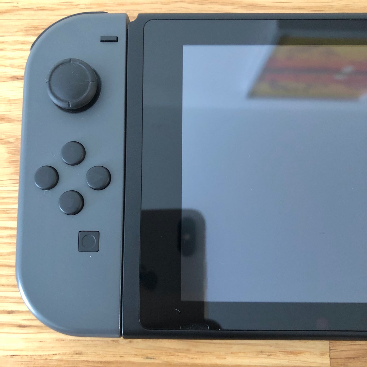 Close-up of grey left Joy-Con on Nintendo Switch, showing D-pad style buttons, stick and capture button.
