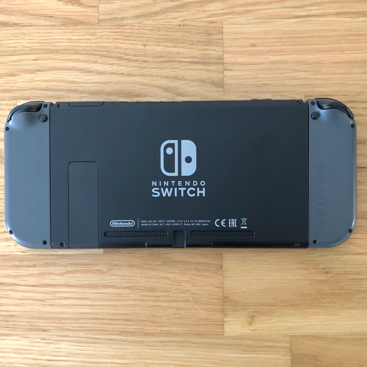 Back of Nintendo Switch console with grey Joy-Cons attached, showing logo, kickstand and trigger buttons laid flat.
