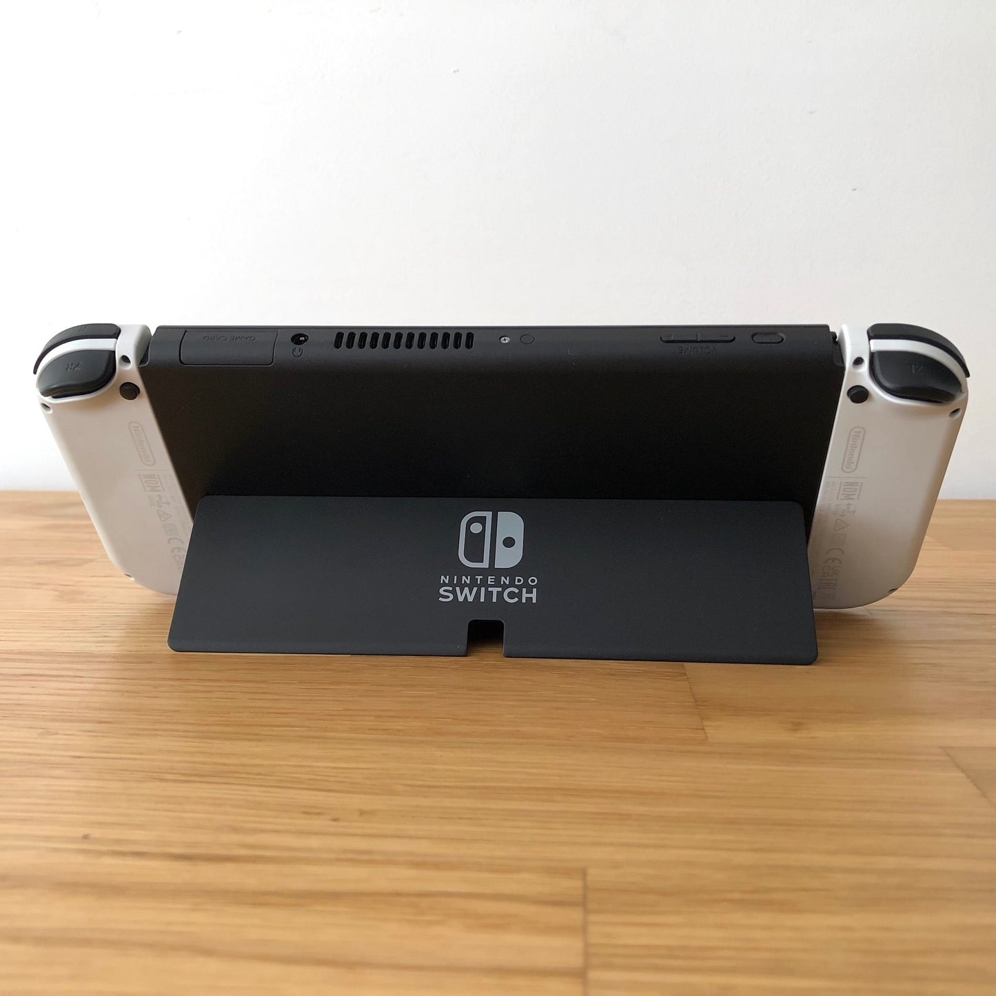 Back of Nintendo Switch OLED with kickstand open, showing logo, game card slot, vent and volume controls.