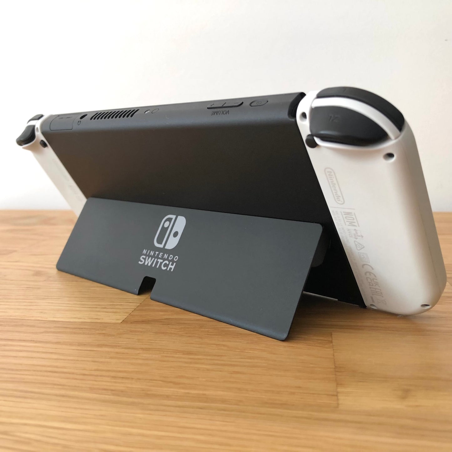 Angled rear view of Nintendo Switch OLED with kickstand open, showing logo, triggers and top-side buttons.