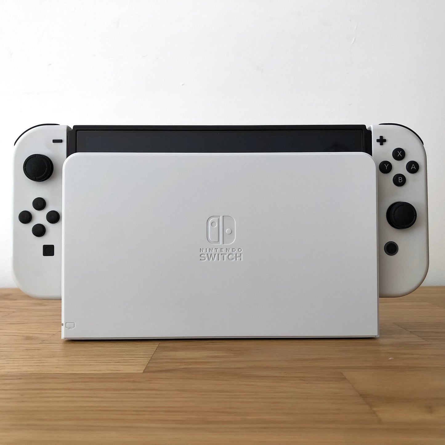 Front of Nintendo Switch OLED console docked, showing white Joy-Cons with button layout visible on both sides.