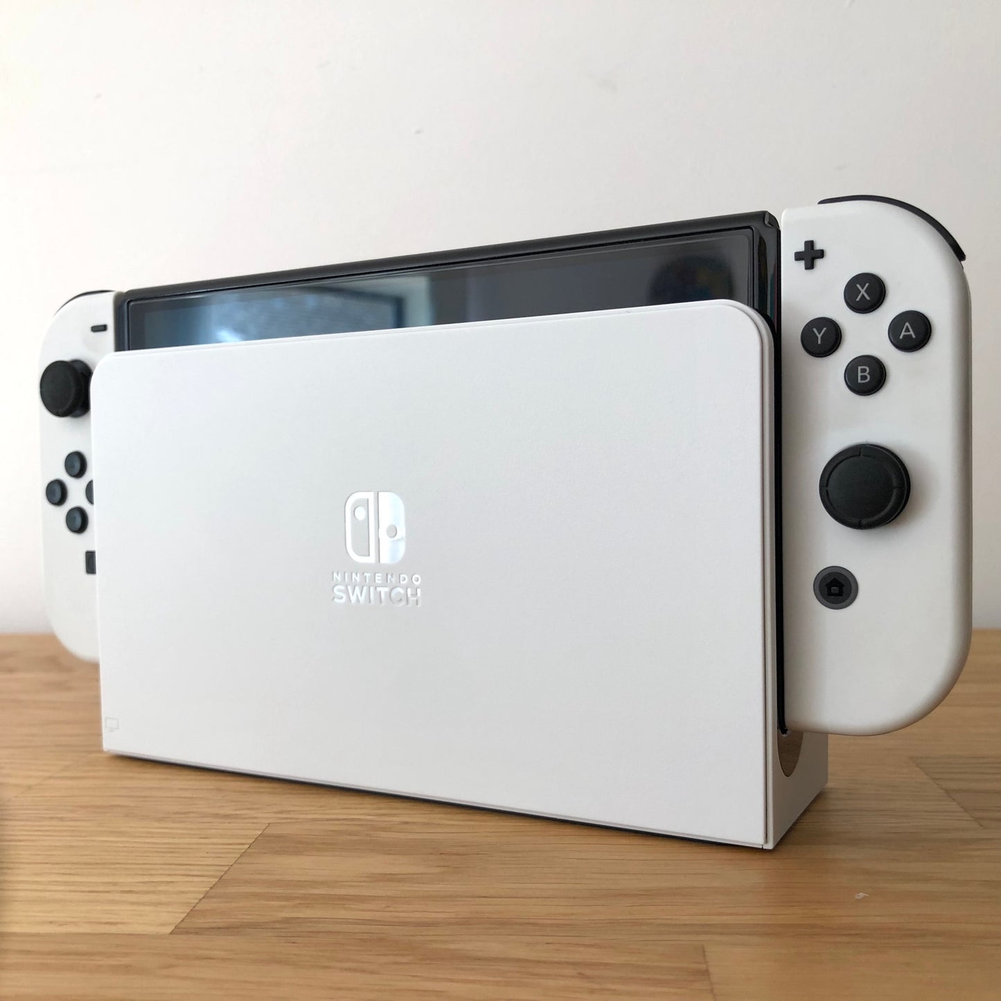 Angled view of Nintendo Switch OLED console docked, showing white Joy-Cons with visible buttons and sticks.