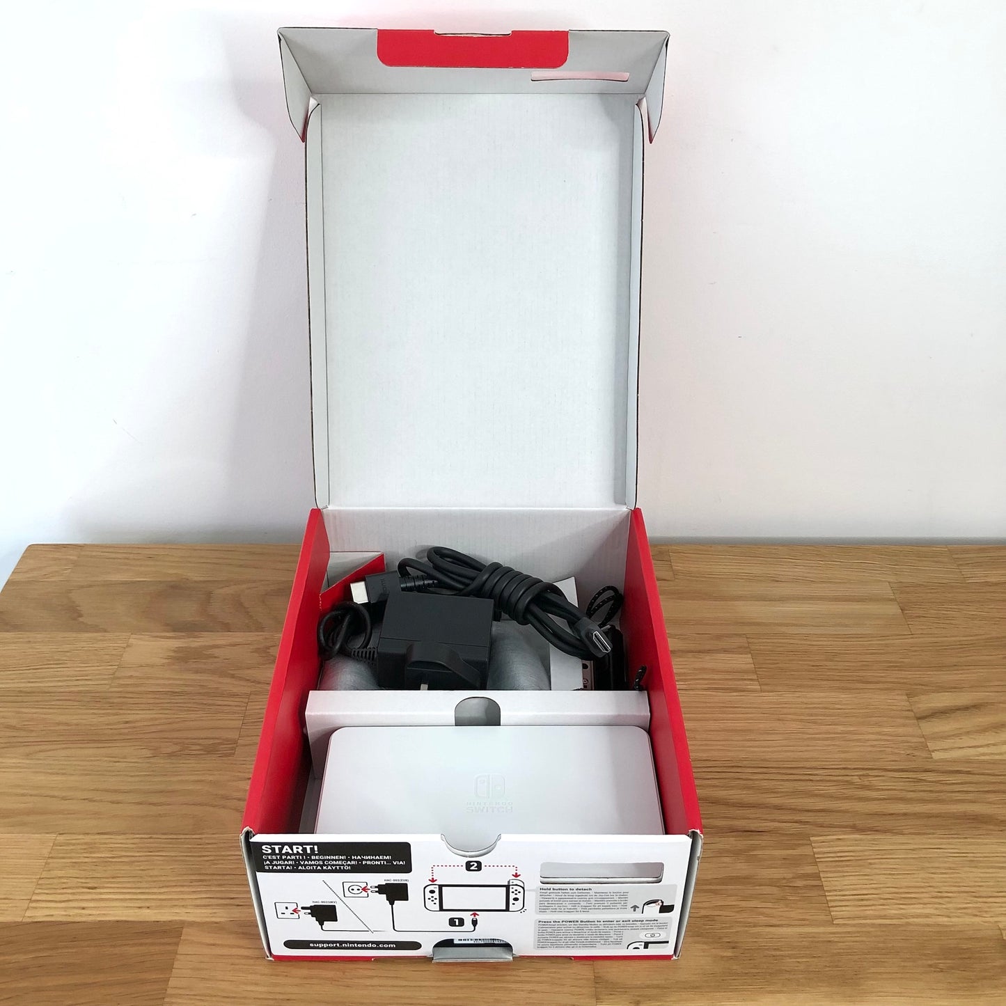 Second layer of Nintendo Switch OLED box showing dock, Joy-Con grip, HDMI cable, charger and straps securely packed.