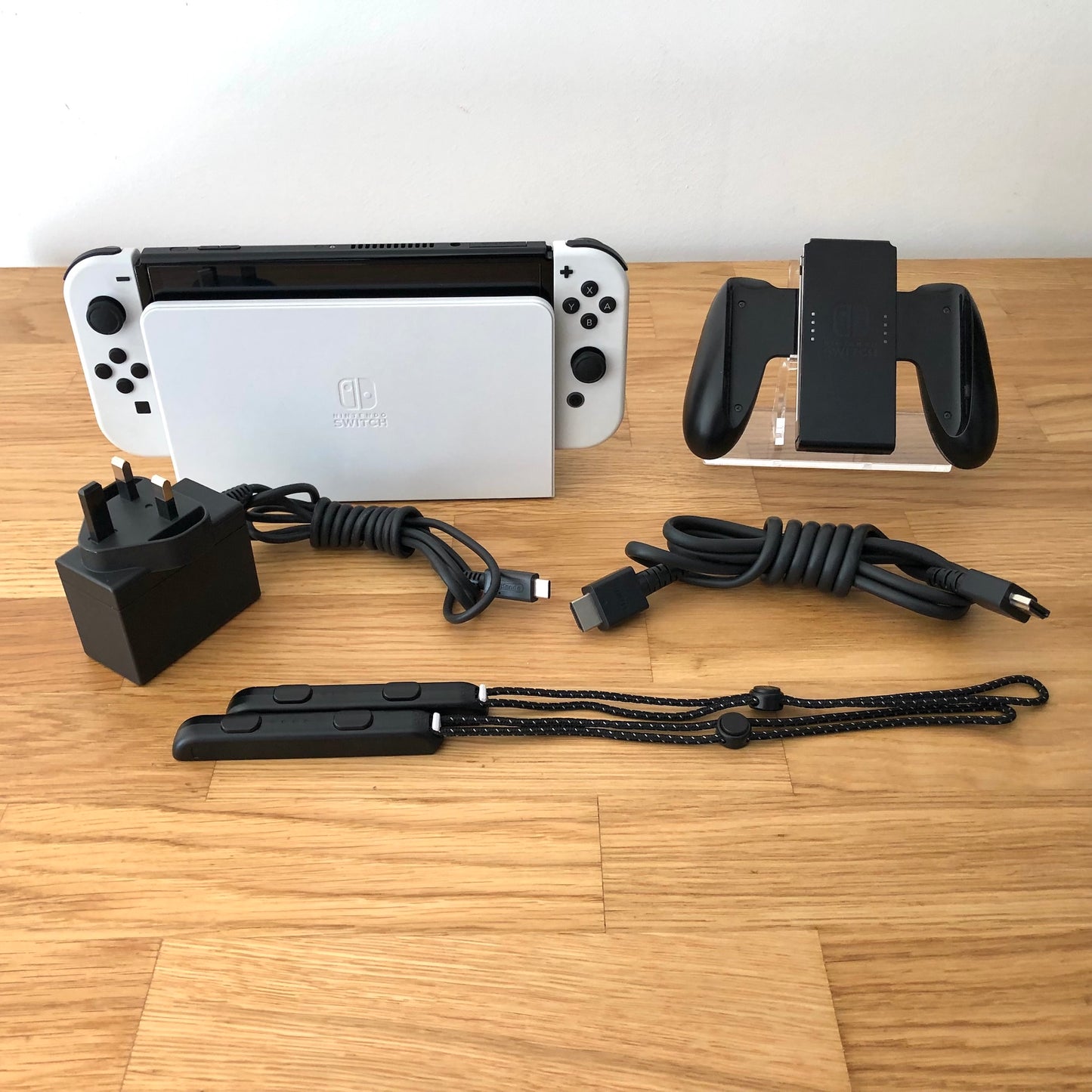 White Nintendo Switch OLED console with charger, HDMI cable, Joy-Con grip and wrist straps laid out.