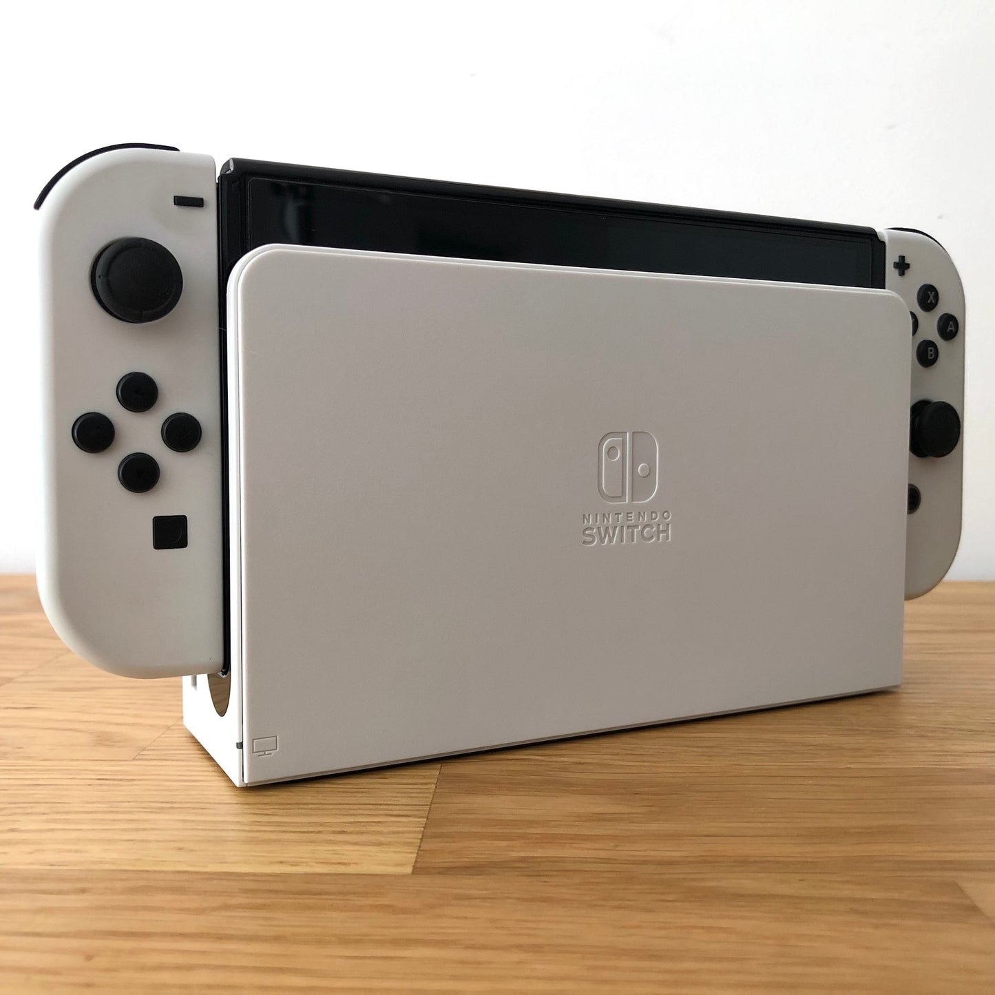Angled view of Nintendo Switch OLED console docked, showing white Joy-Cons with visible buttons and sticks.