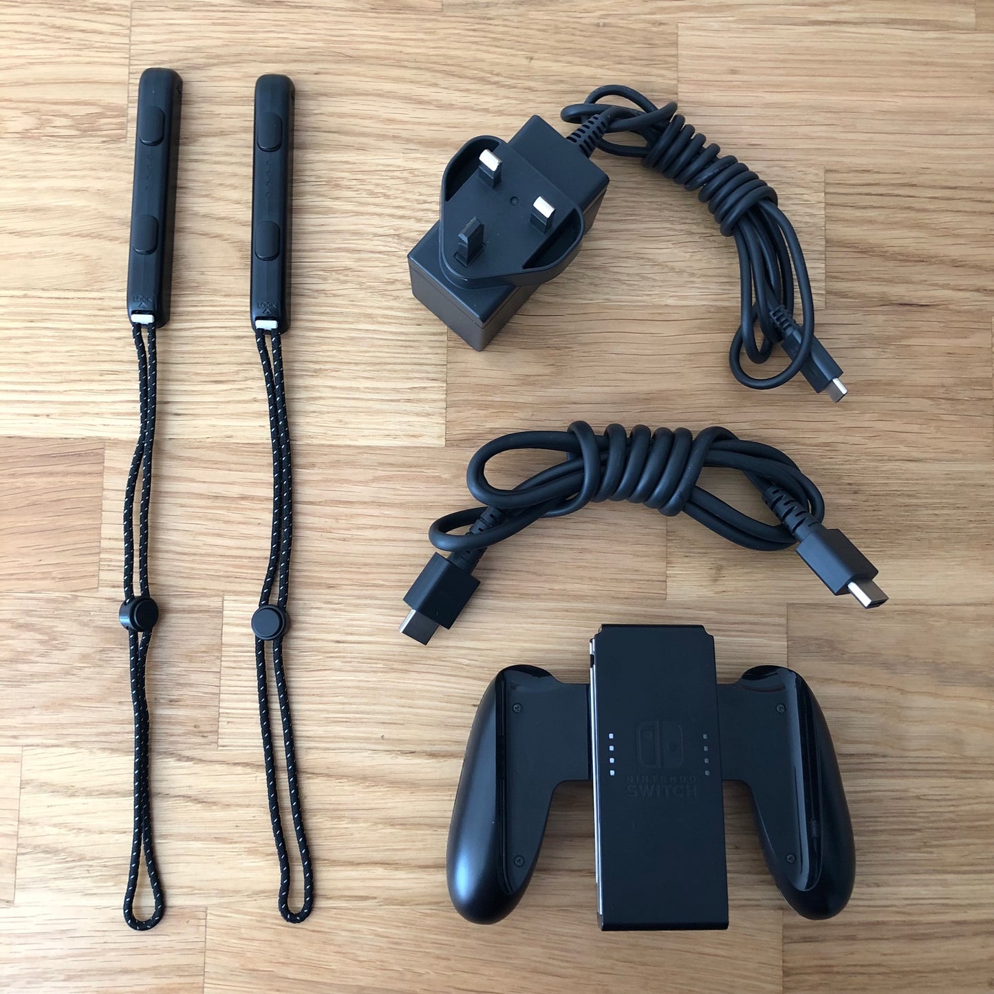 Nintendo Switch OLED accessories including Joy-Con straps, HDMI cable, charger plug and Joy-Con grip laid out.