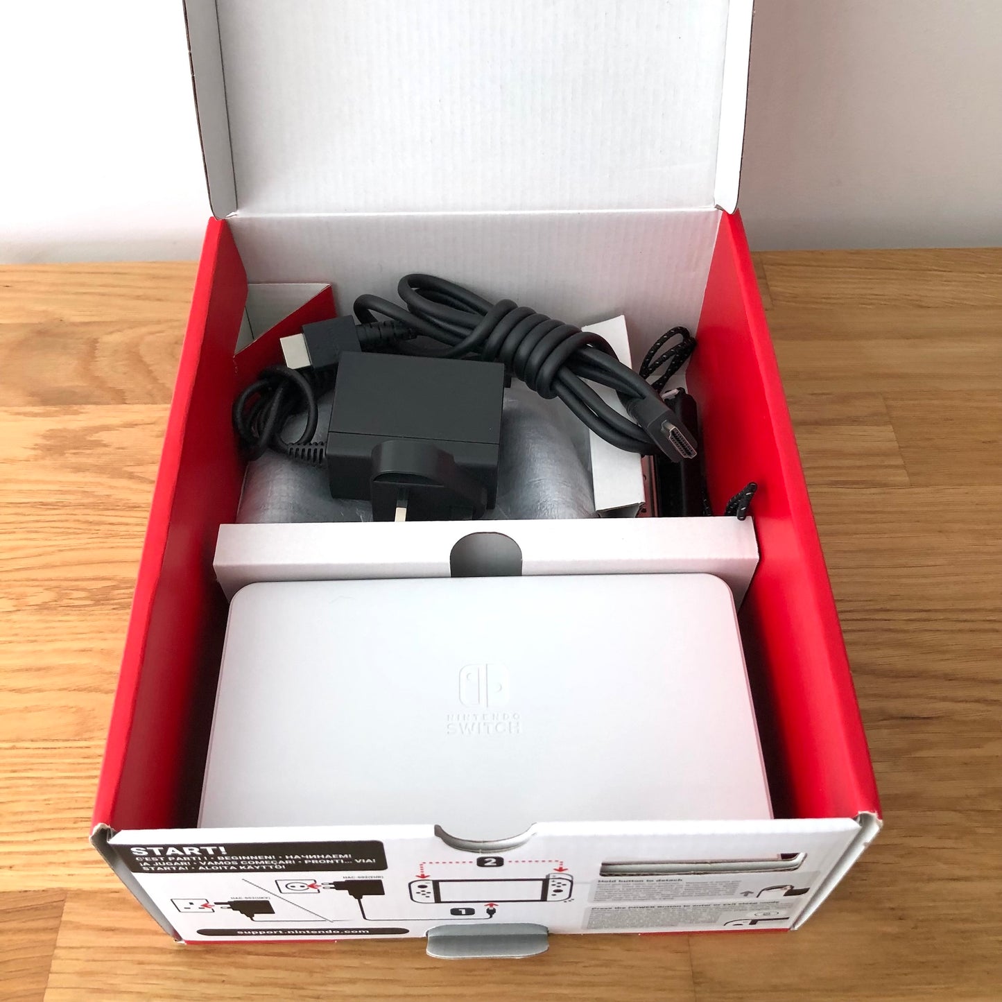 Second layer of Nintendo Switch OLED box showing dock, Joy-Con grip, HDMI cable, charger and straps securely packed.