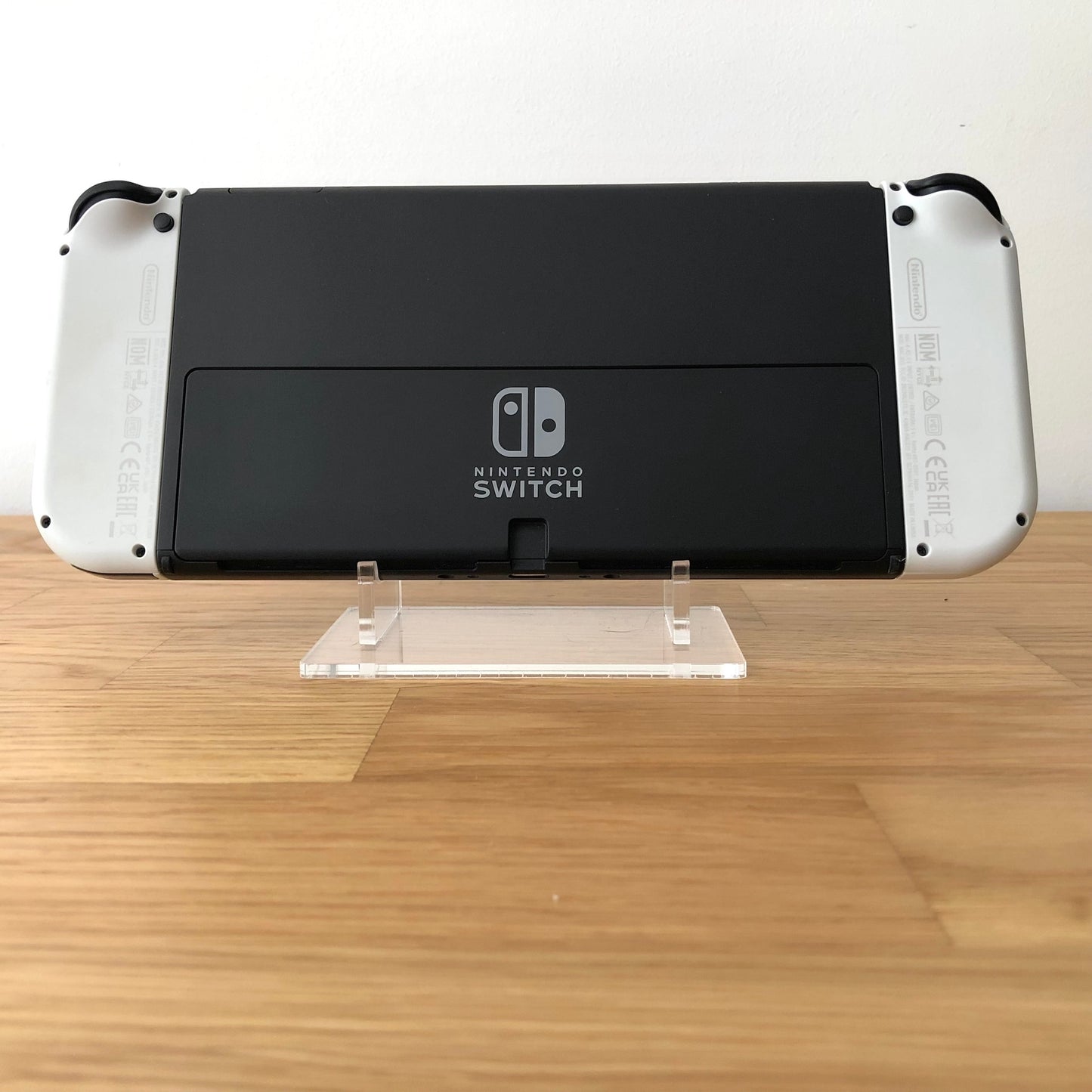 Back of Nintendo Switch OLED console with white Joy-Cons attached, showing logo and rear casing detail.