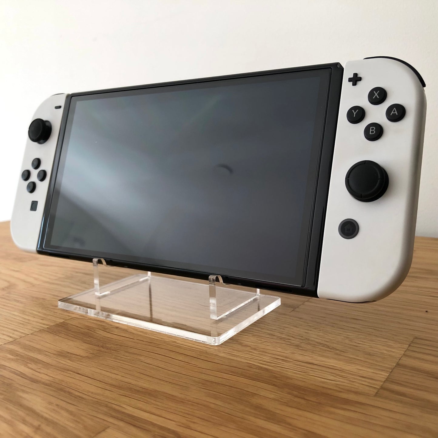 Angled front view of Nintendo Switch OLED console with white Joy-Cons attached, screen off, on display stand.