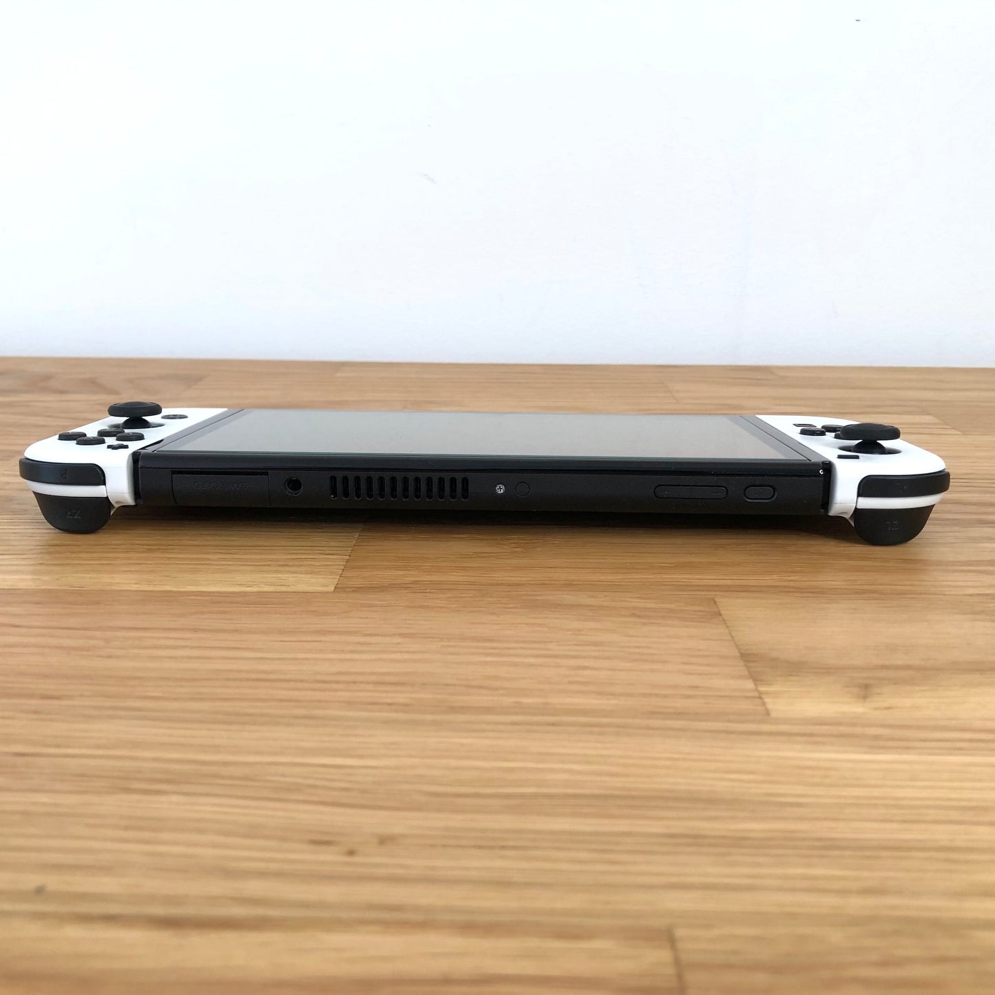 Back of Nintendo Switch OLED console with white Joy-Cons shown flat on table, logo and kickstand visible.