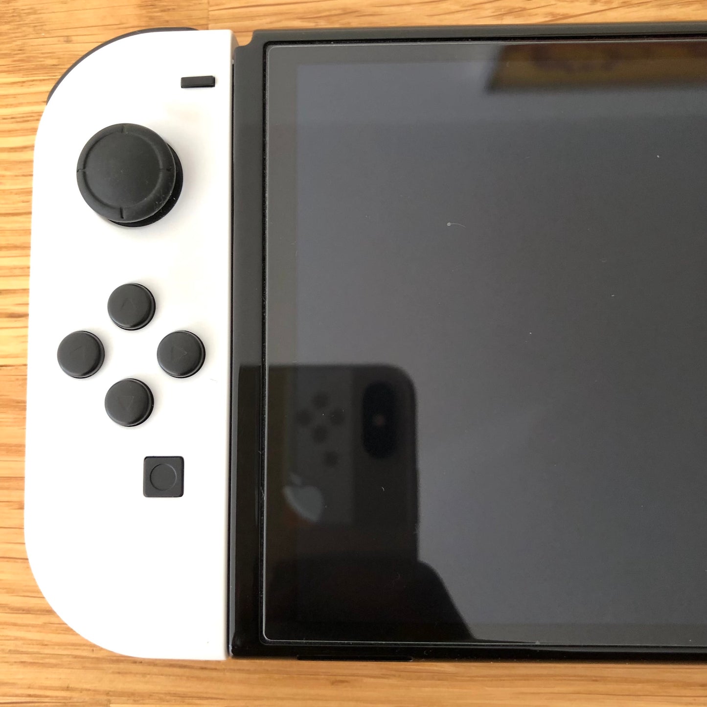 Close-up of left side of Nintendo Switch OLED screen with white Joy-Con showing control stick and buttons.