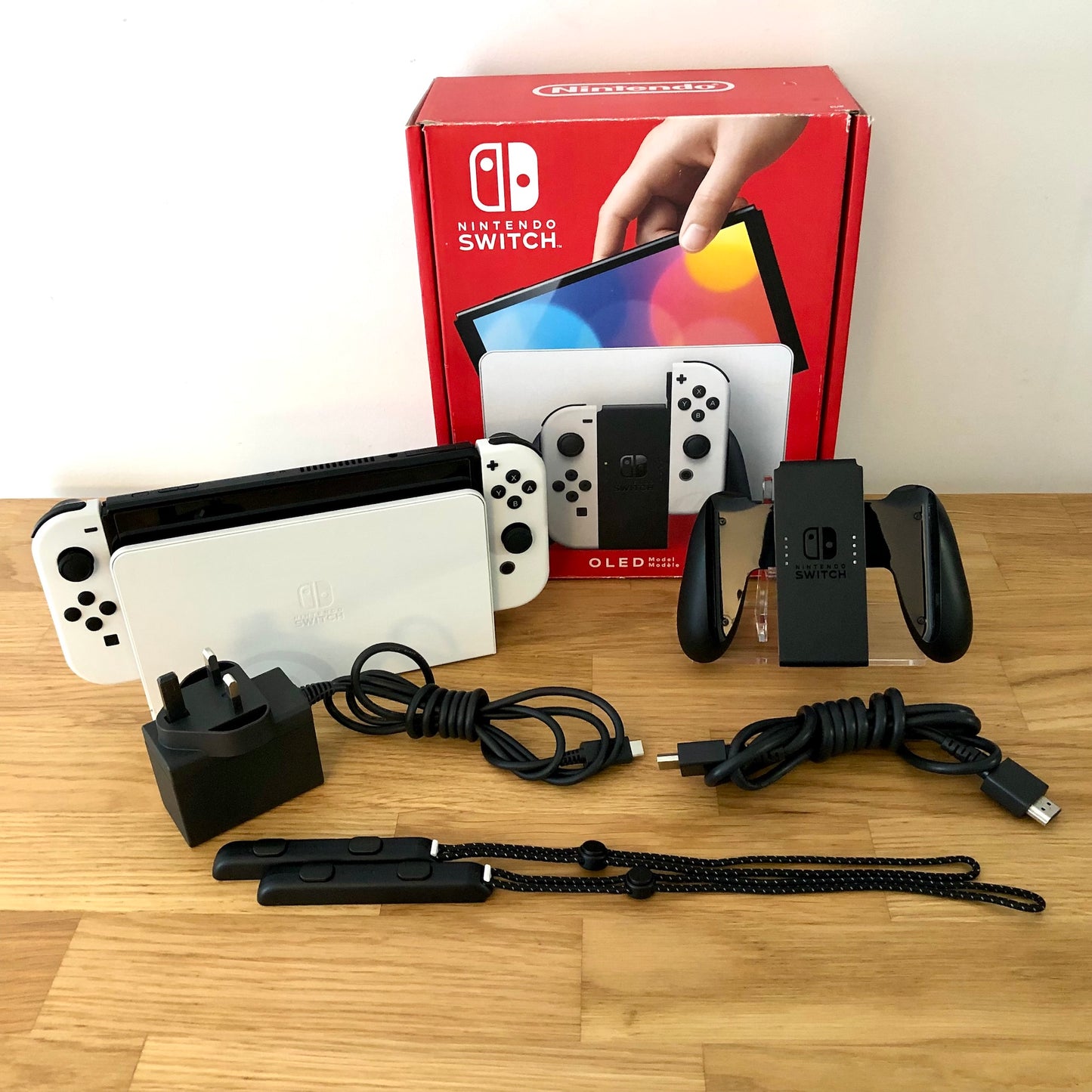 White Nintendo Switch OLED console with original box, Joy-Con grip, charger, HDMI cable and straps included.”