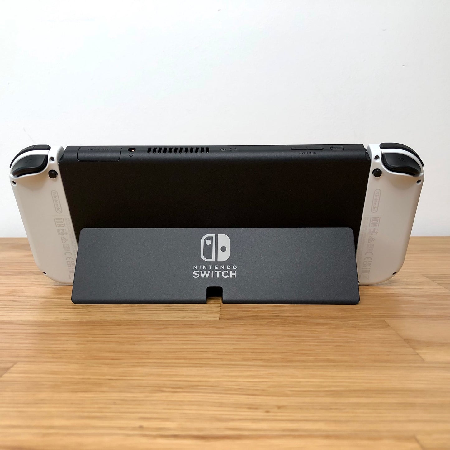 Back of Nintendo Switch OLED with kickstand open, showing logo, game card slot, vent and volume controls.