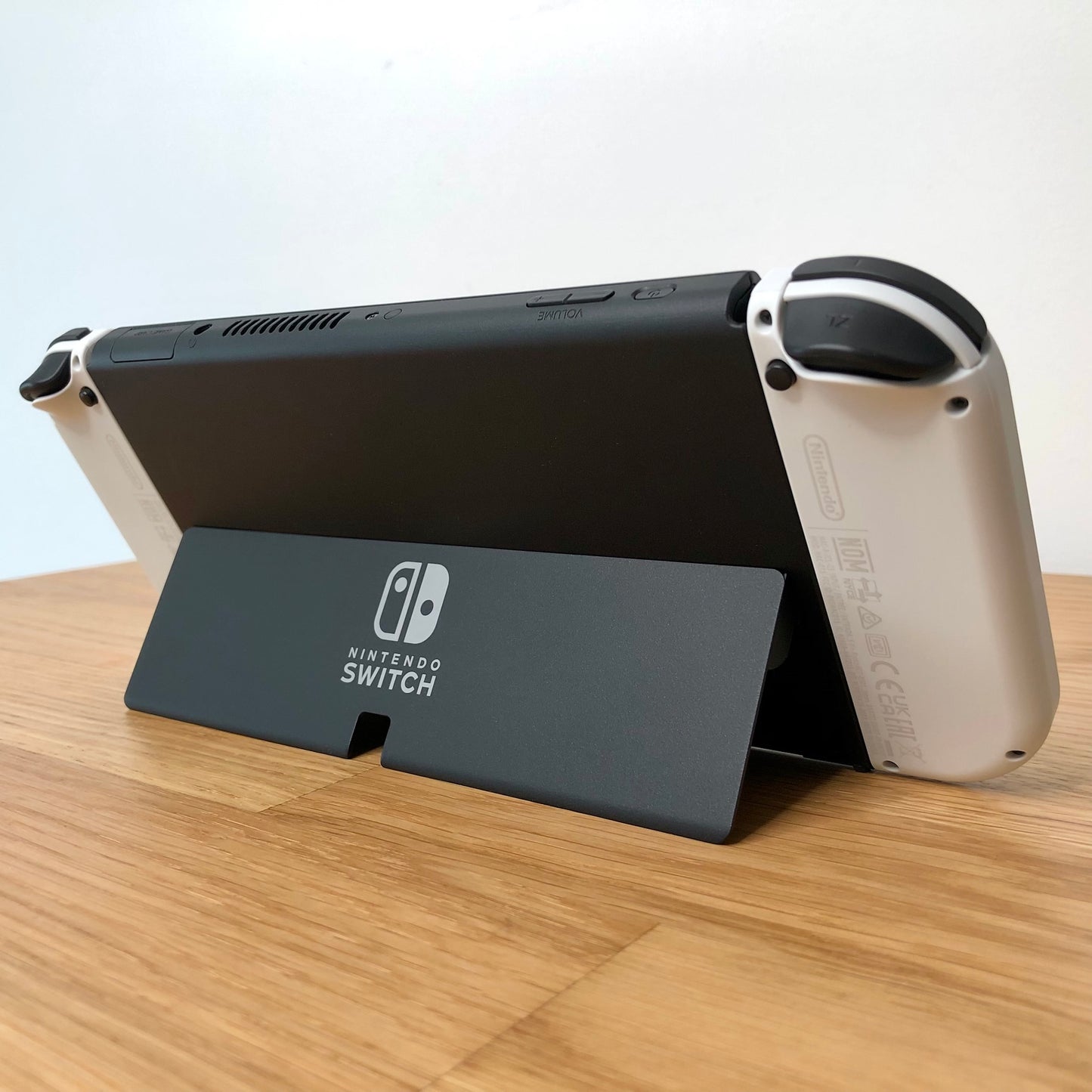 Angled rear view of Nintendo Switch OLED with kickstand open, showing logo, triggers and top-side buttons.
