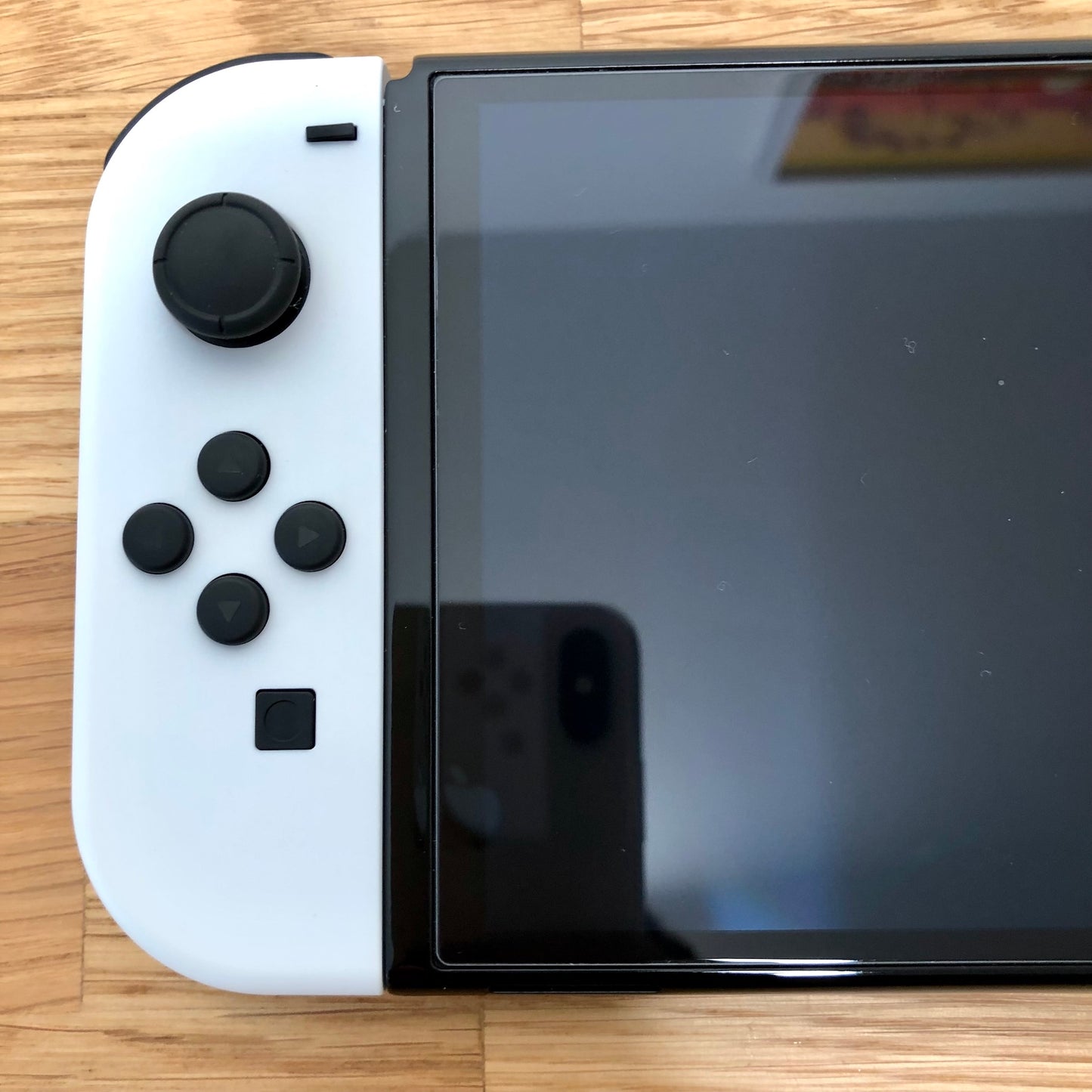 Close-up of white left Joy-Con on Nintendo Switch OLED, showing D-pad style buttons, left stick and minus button.