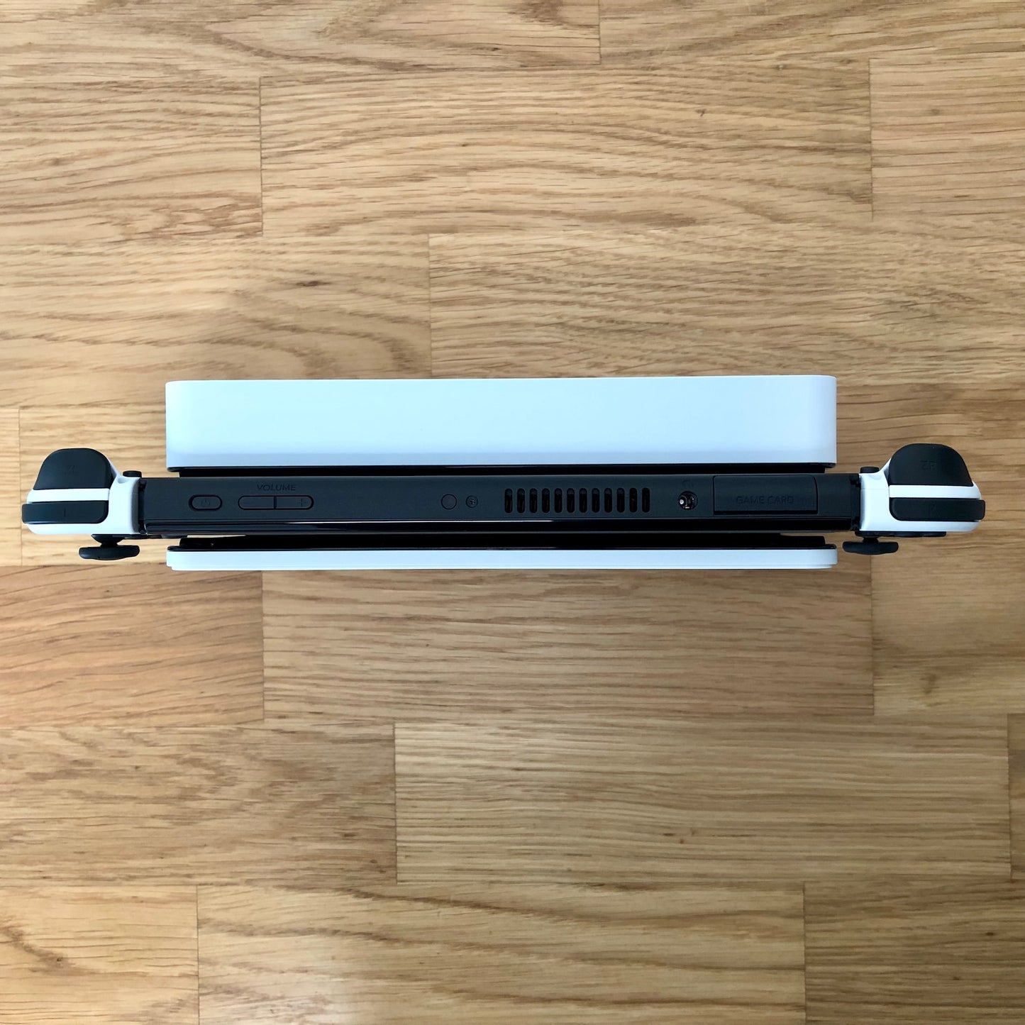 op-down view of Nintendo Switch OLED in dock, showing Joy-Con triggers, game card slot and top-side buttons.